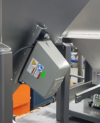 Caja de control de máquina industrial montada sobre equipo gris, con etiquetas de advertencia y panel naranja cerca