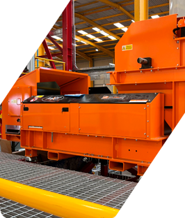 Máquina industrial naranja en una fábrica, con suelo de rejilla metálica y vigas superiores.