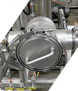 Válvula industrial de acero inoxidable con escotilla circular y tuberías en un entorno de fábrica.