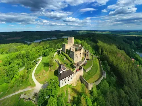Castle on a hill surrounded by lush green trees and a blue sky with clouds.