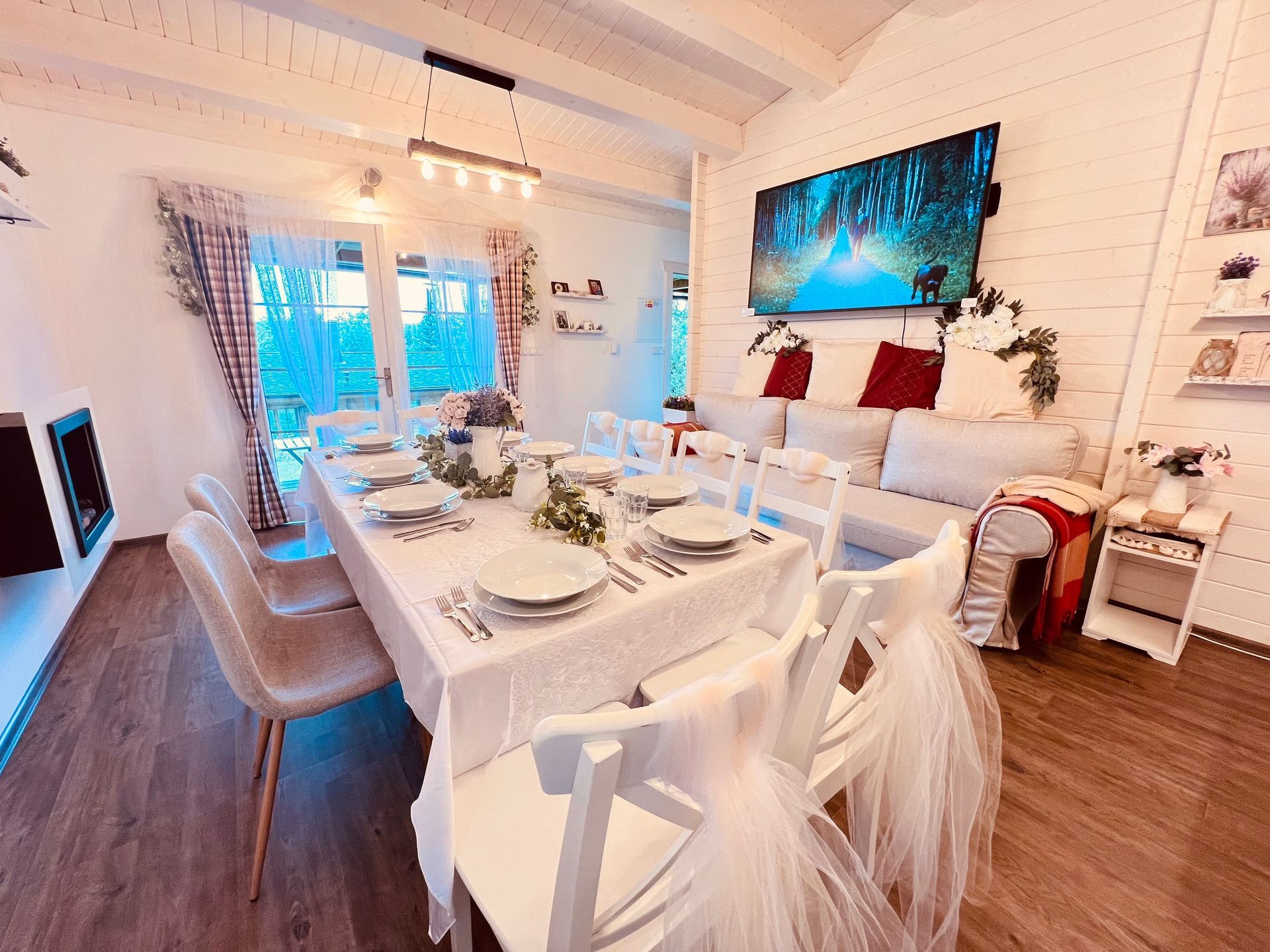 Dining room with a long, white-clothed table set for a meal; white chairs and a white sofa.