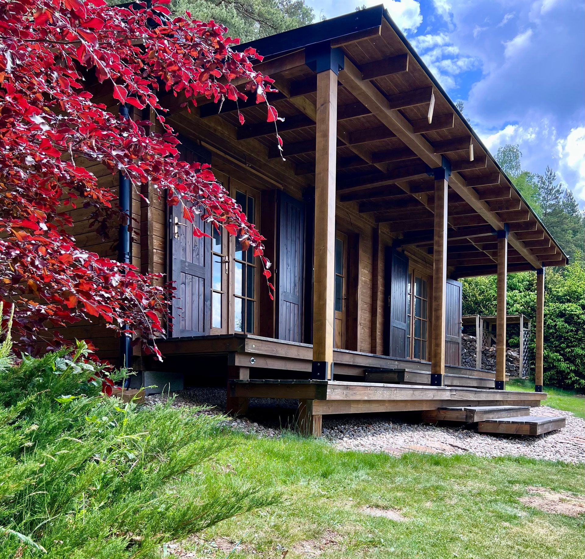 Wooden cabin with porch; red tree on left, green grass in front.