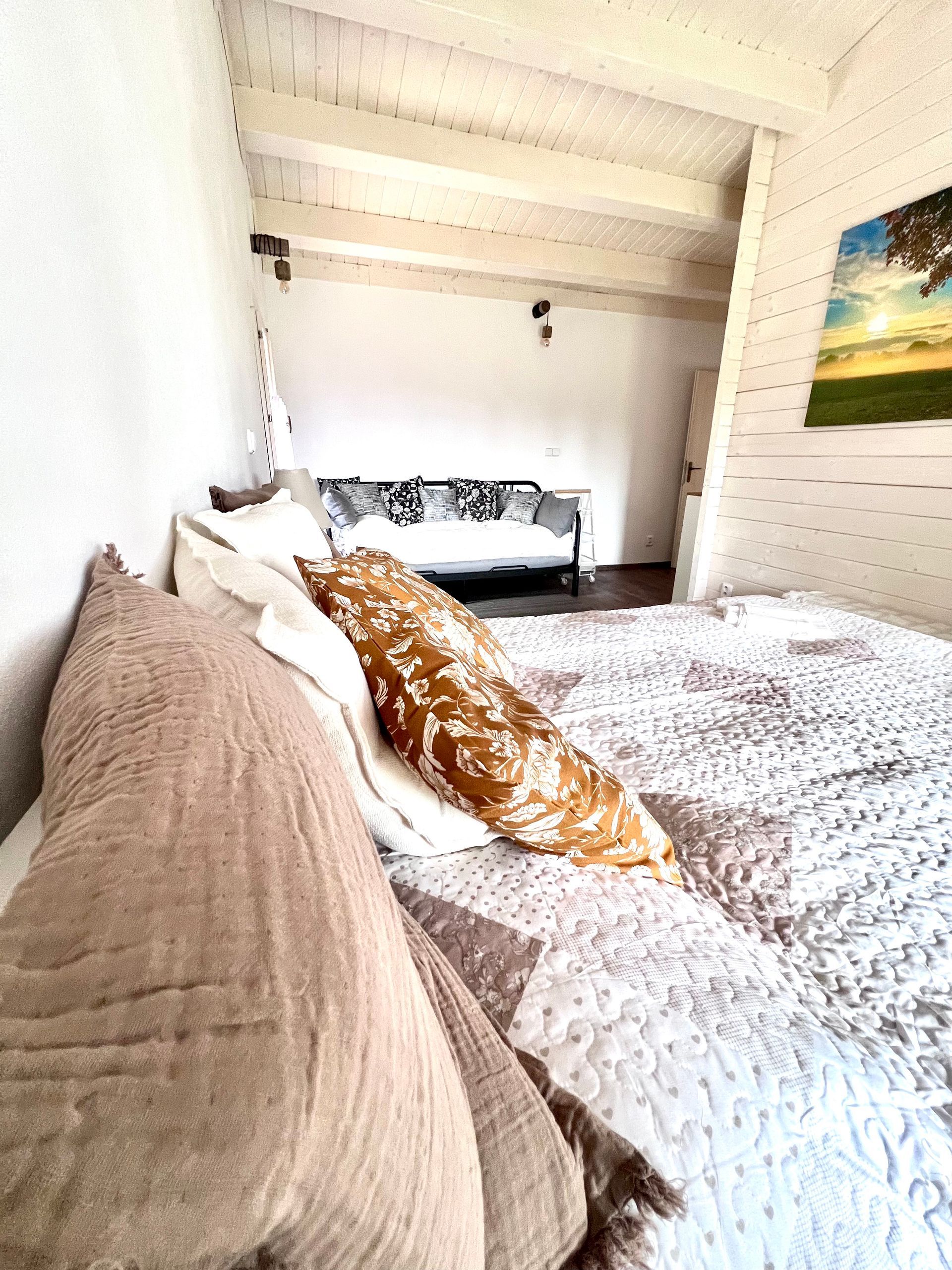 Bedroom with bed, pillows, and a decorative sofa, white ceiling and wall, painting on the wall.