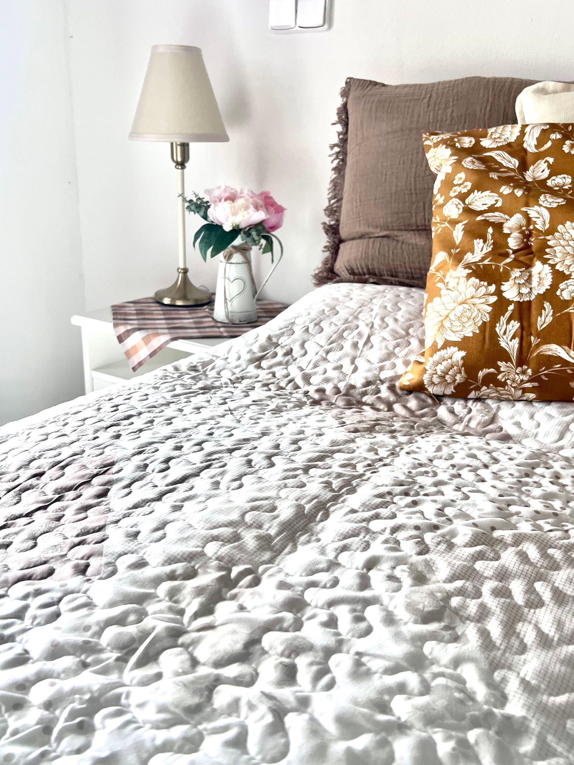 Bedroom with textured white quilt, bedside lamp, and decorative pillows.