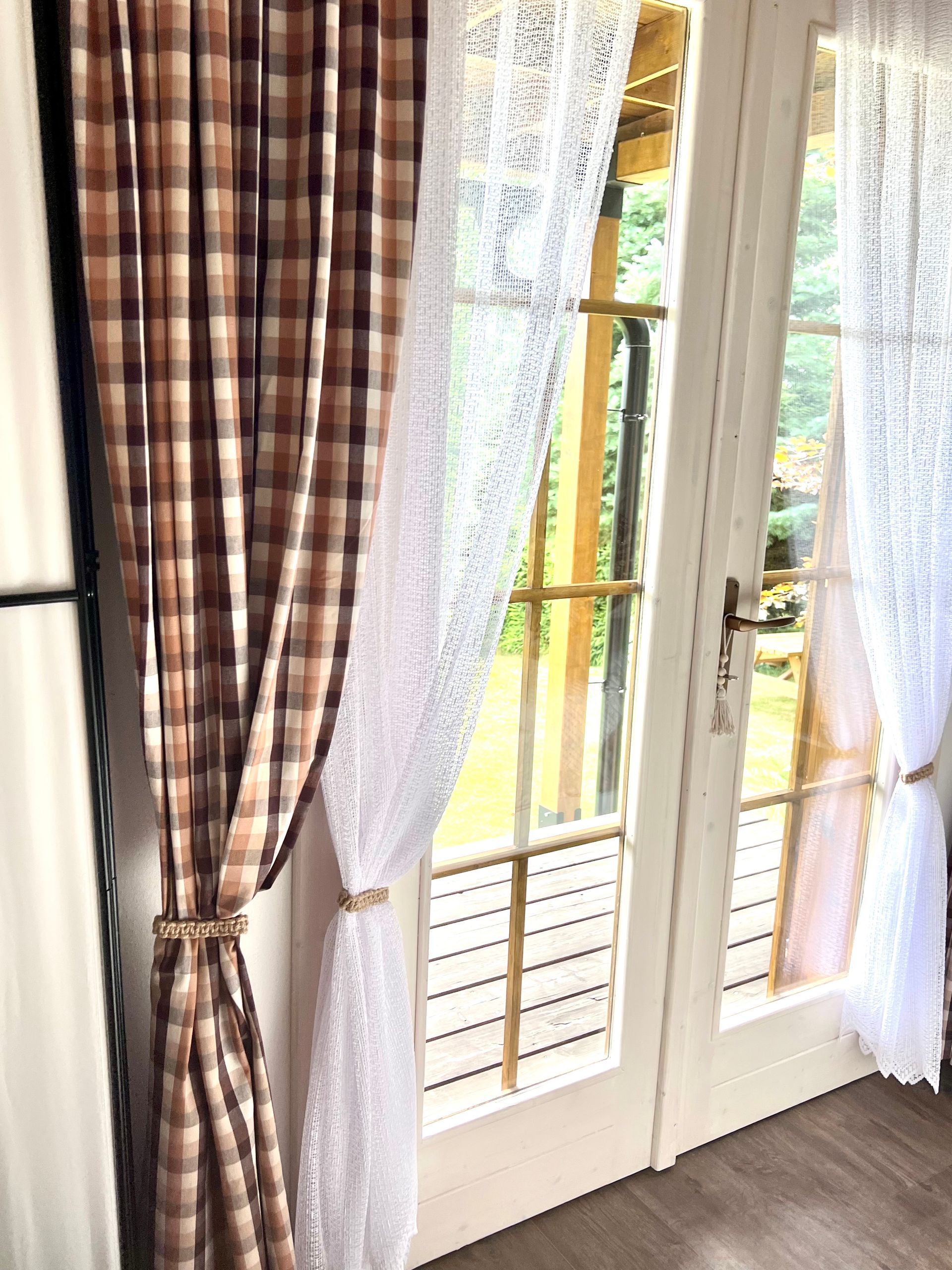 Brown plaid curtain with a white lace curtain over a glass door.