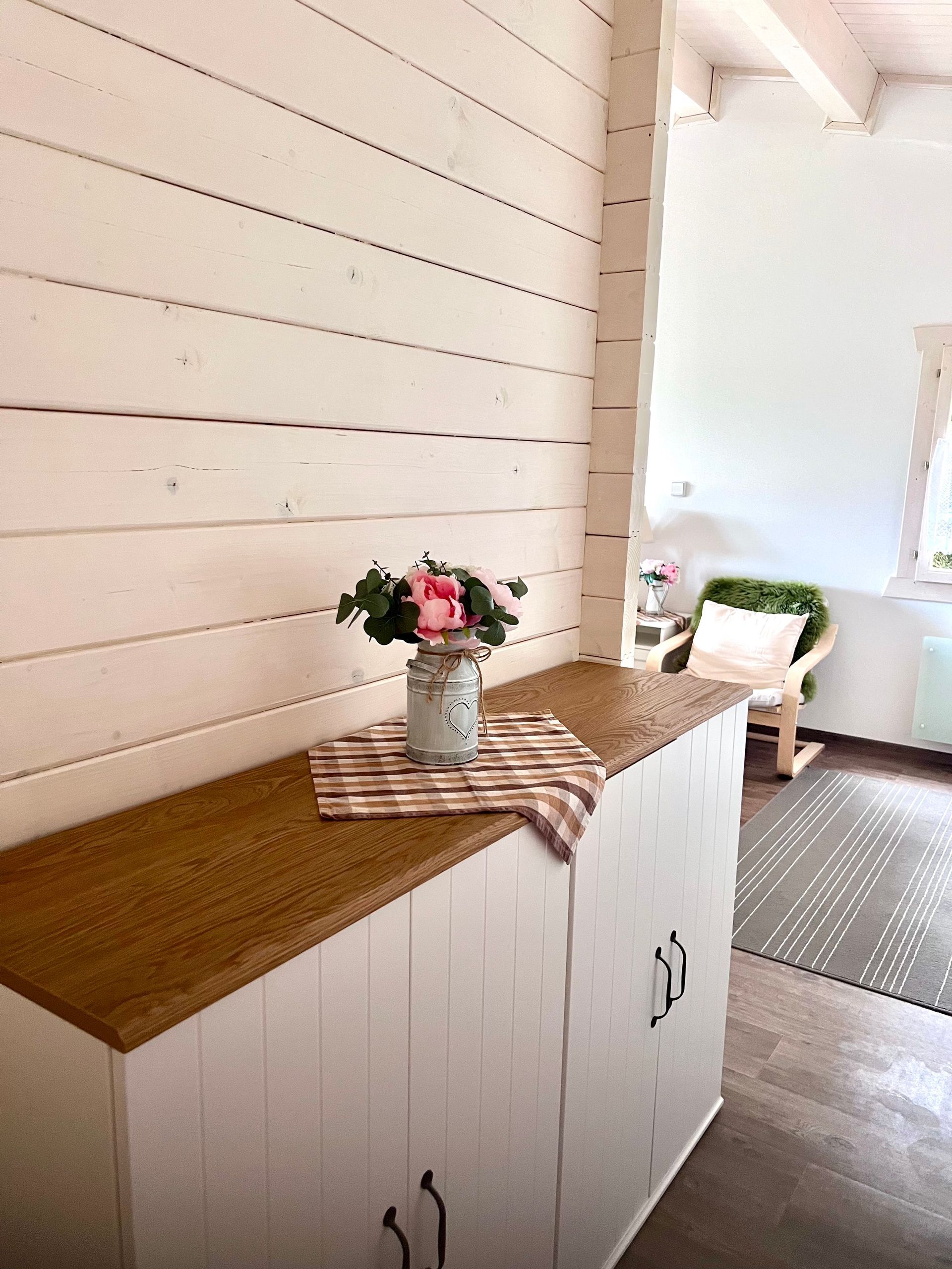 Wooden cabinet with flowers on top, next to a white wood-paneled wall.