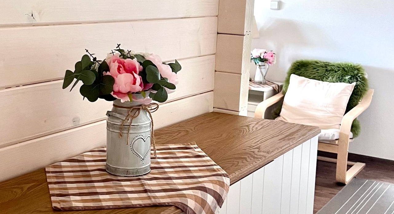 A rustic interior with a floral arrangement, checkered cloth, and wooden chair with pillow.