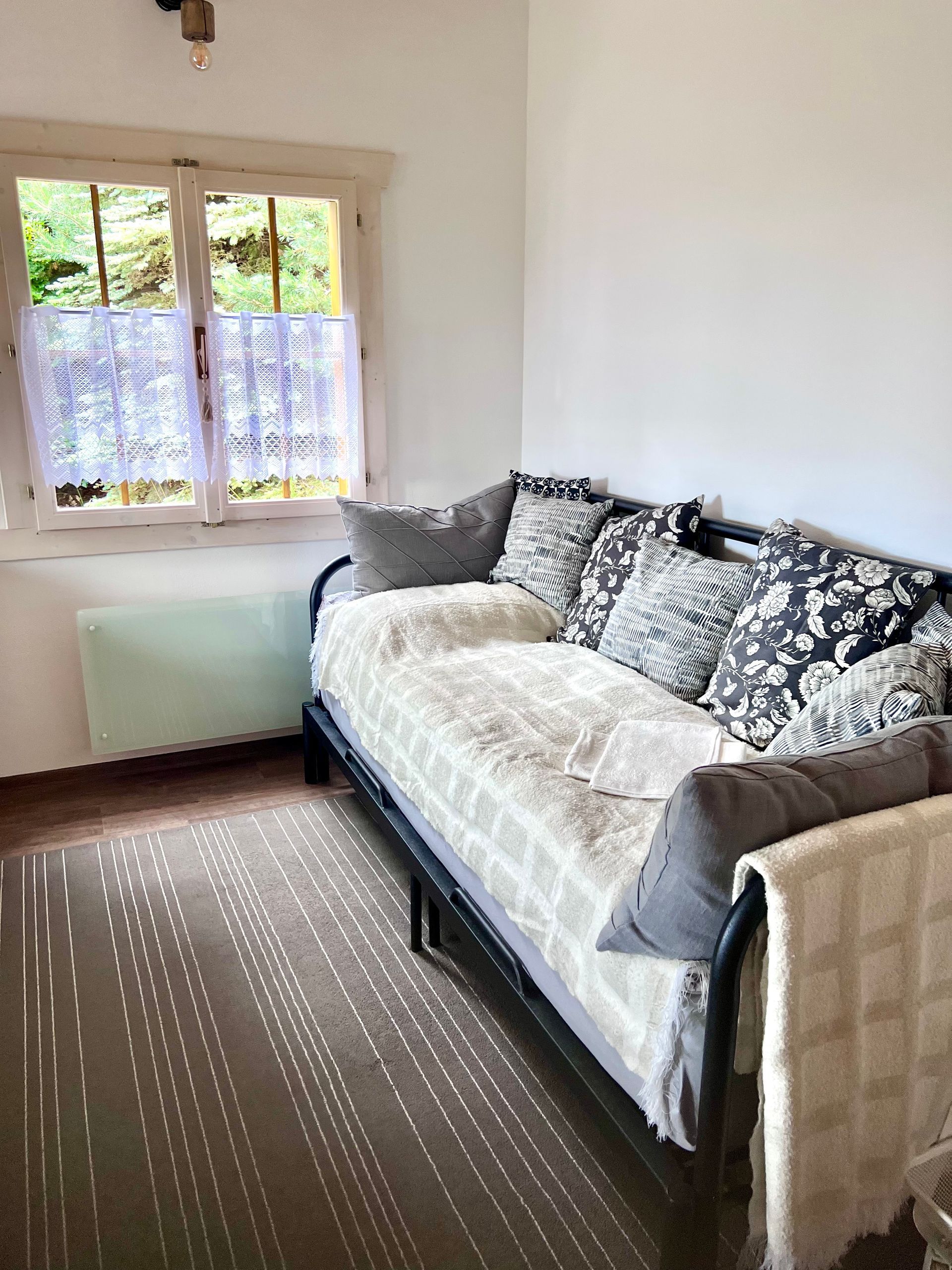 A cozy room with a daybed, window, and patterned rug. Soft light and neutral tones create a calming atmosphere.