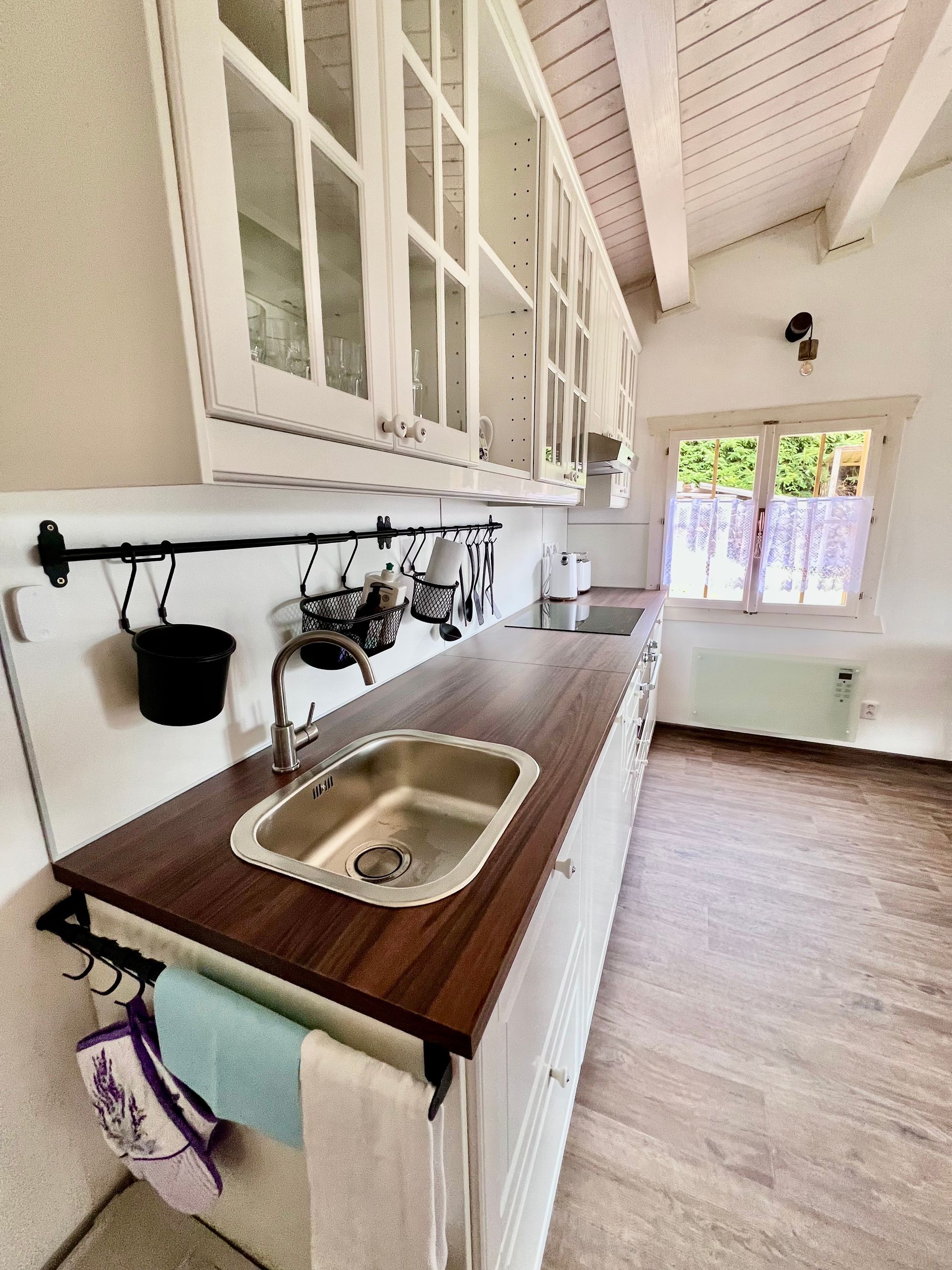 Kitchen with white cabinets, wooden countertop, stainless steel sink, and small window.