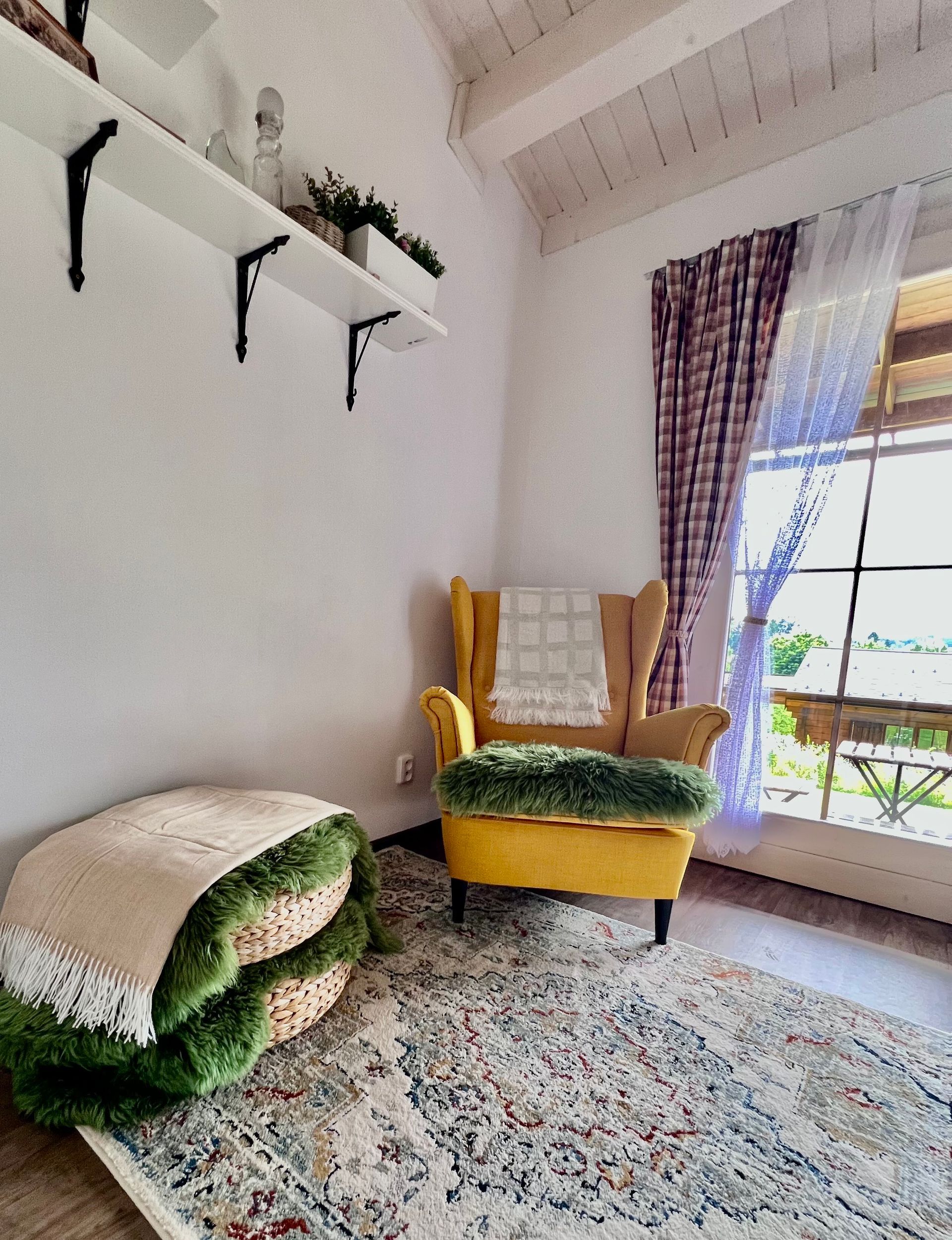 Cozy reading nook with a yellow armchair, patterned rug, and layered textured floor cushions by a window with a view.