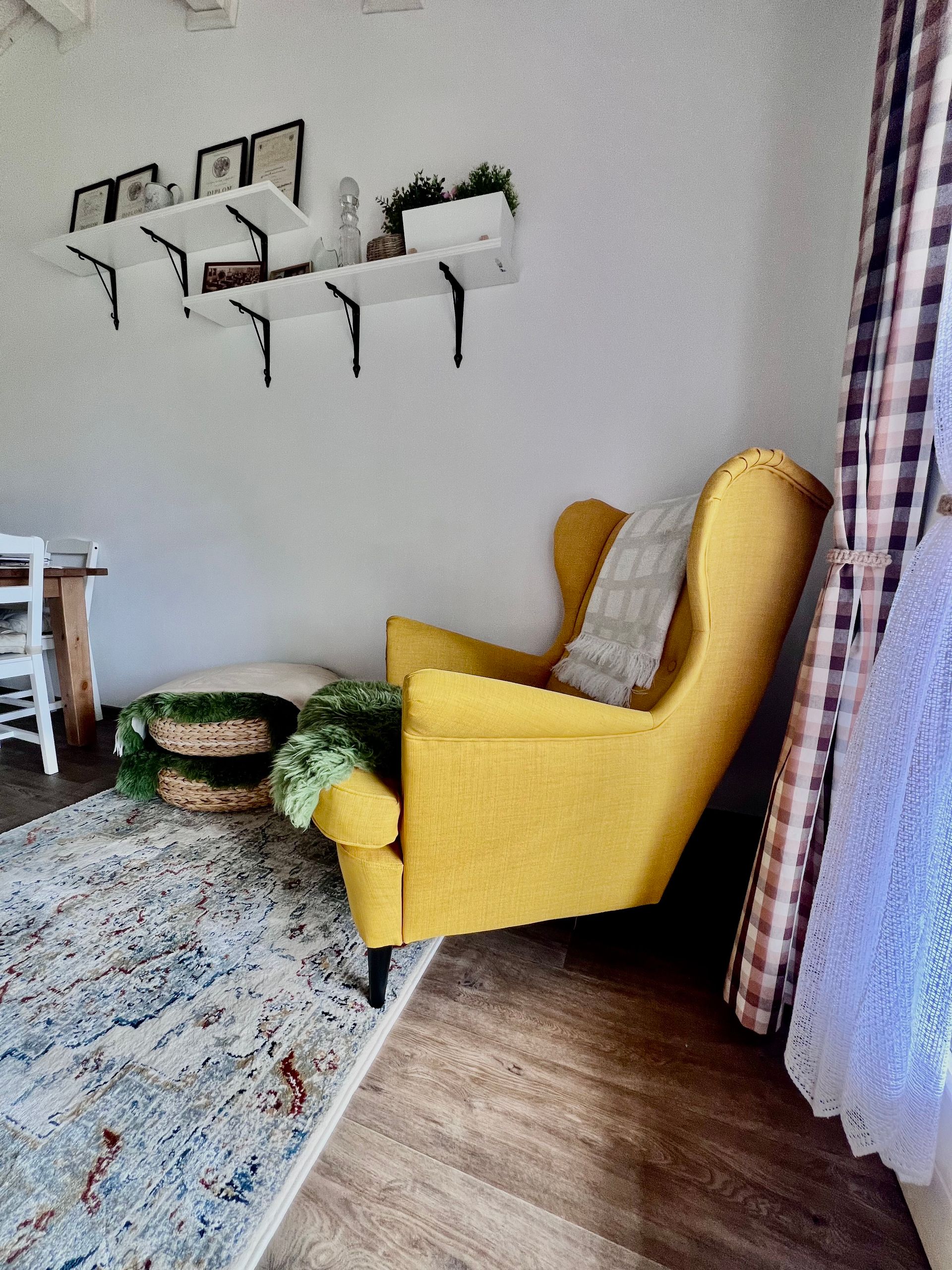 Yellow armchair in a room with shelves, rug, and woven basket. Checkered curtain on right.