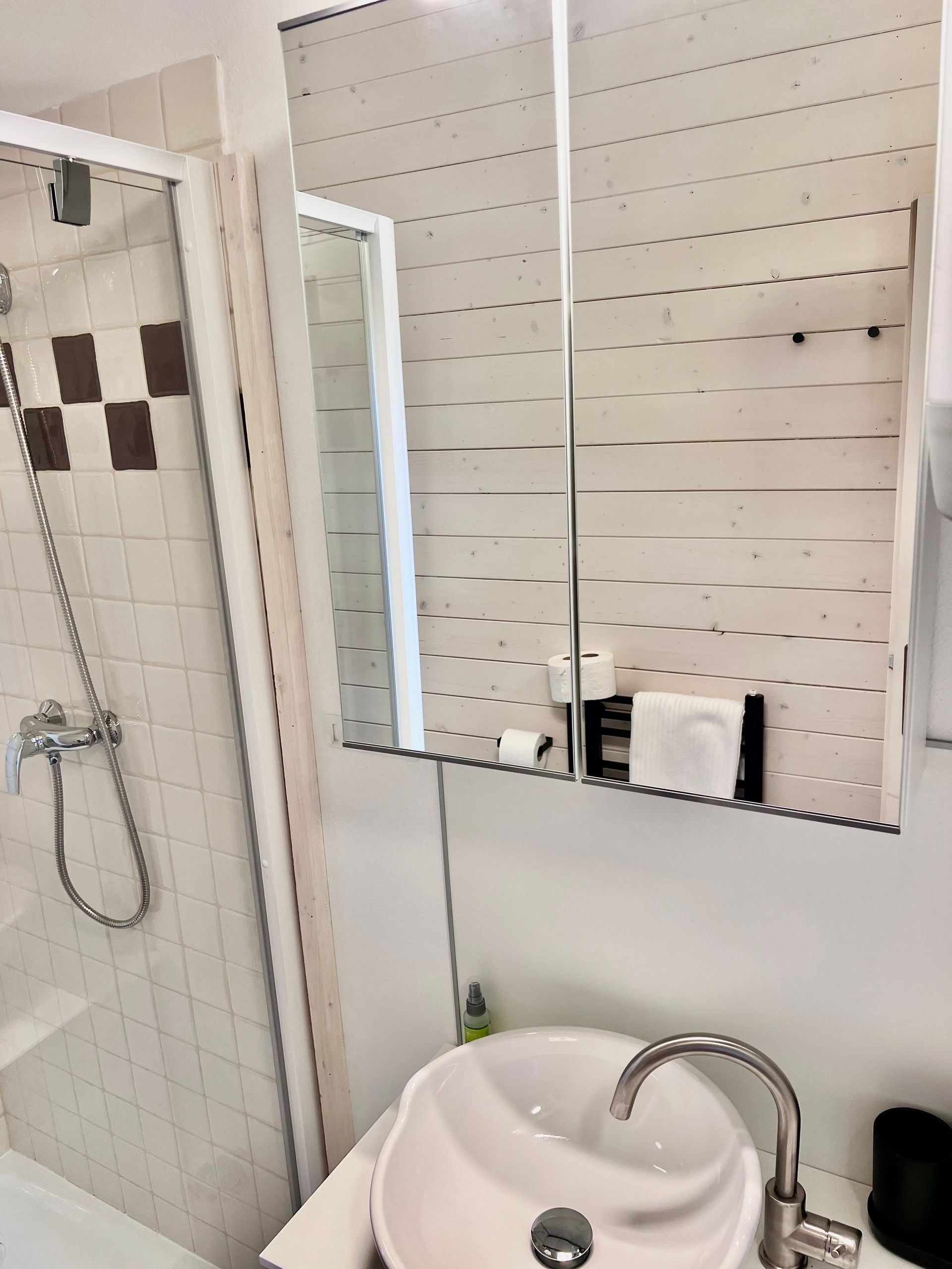 Bathroom with a sink, mirror, shower, and white and brown tiles.