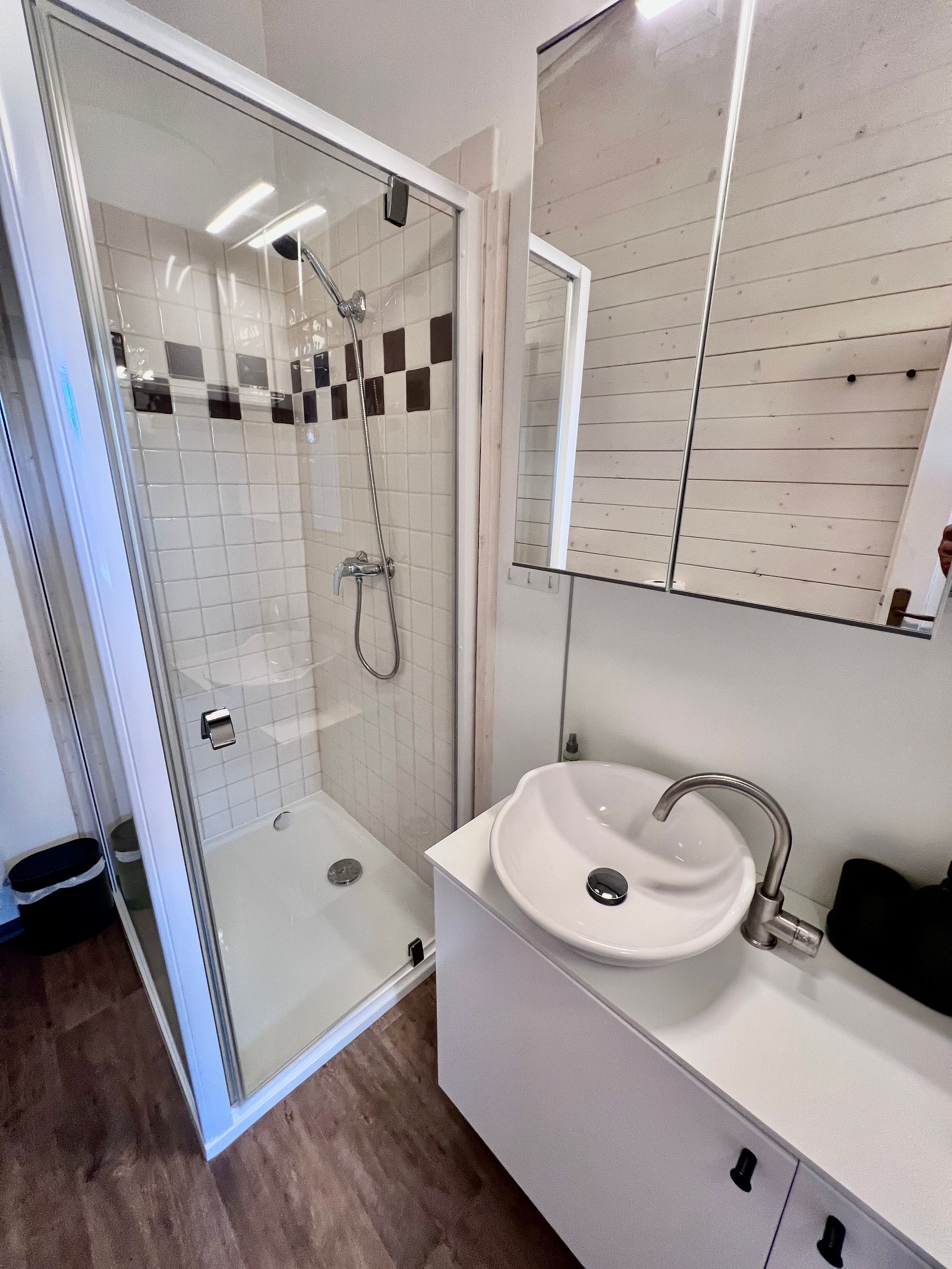 Bathroom with shower, sink, and white cabinets. Shower has glass door with black and white tile accents.