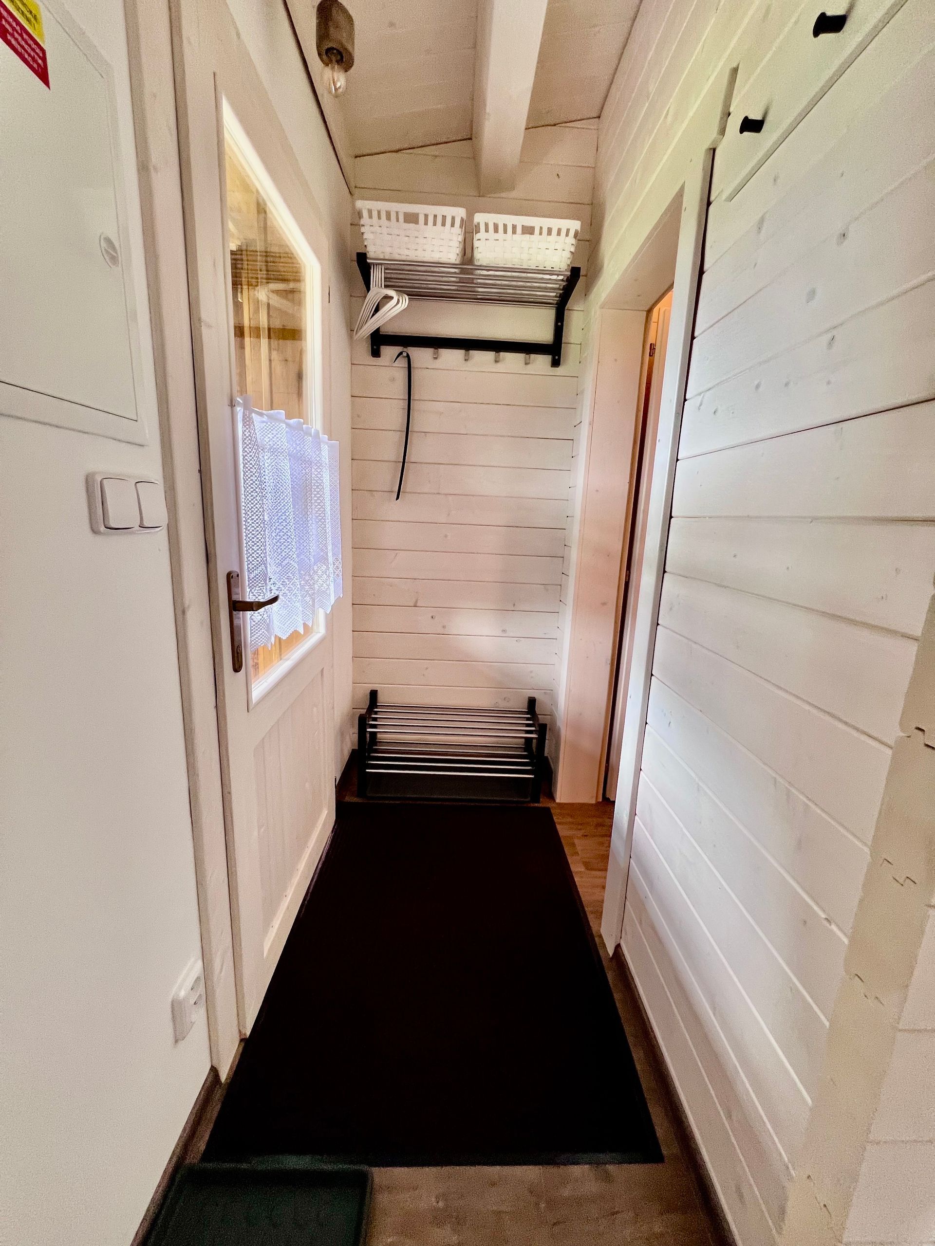 Narrow hallway with a dark rug, white walls, a window, and a bench.