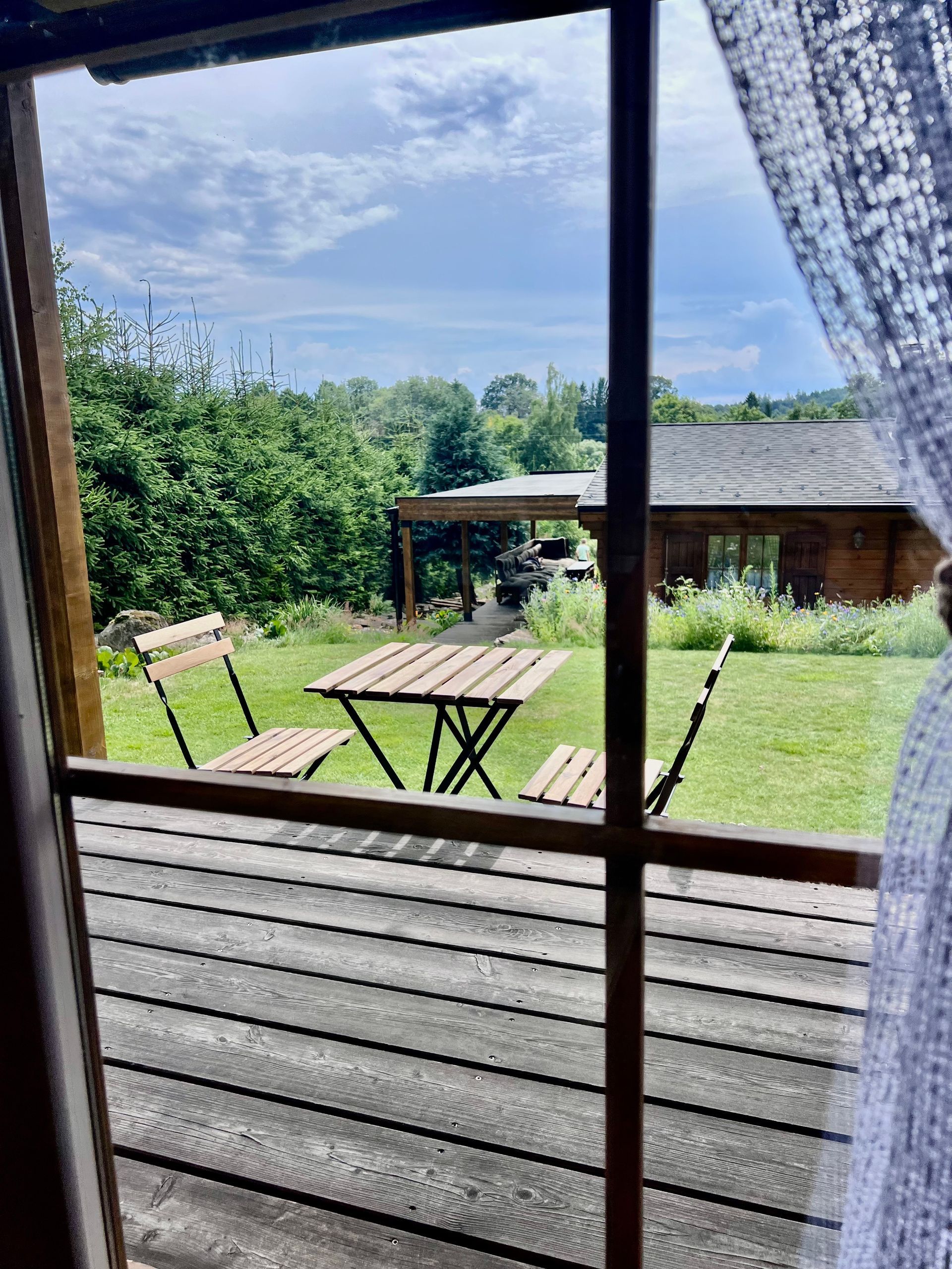 View through a window of a small table and chairs on a lawn, a building in the background, sunny day.