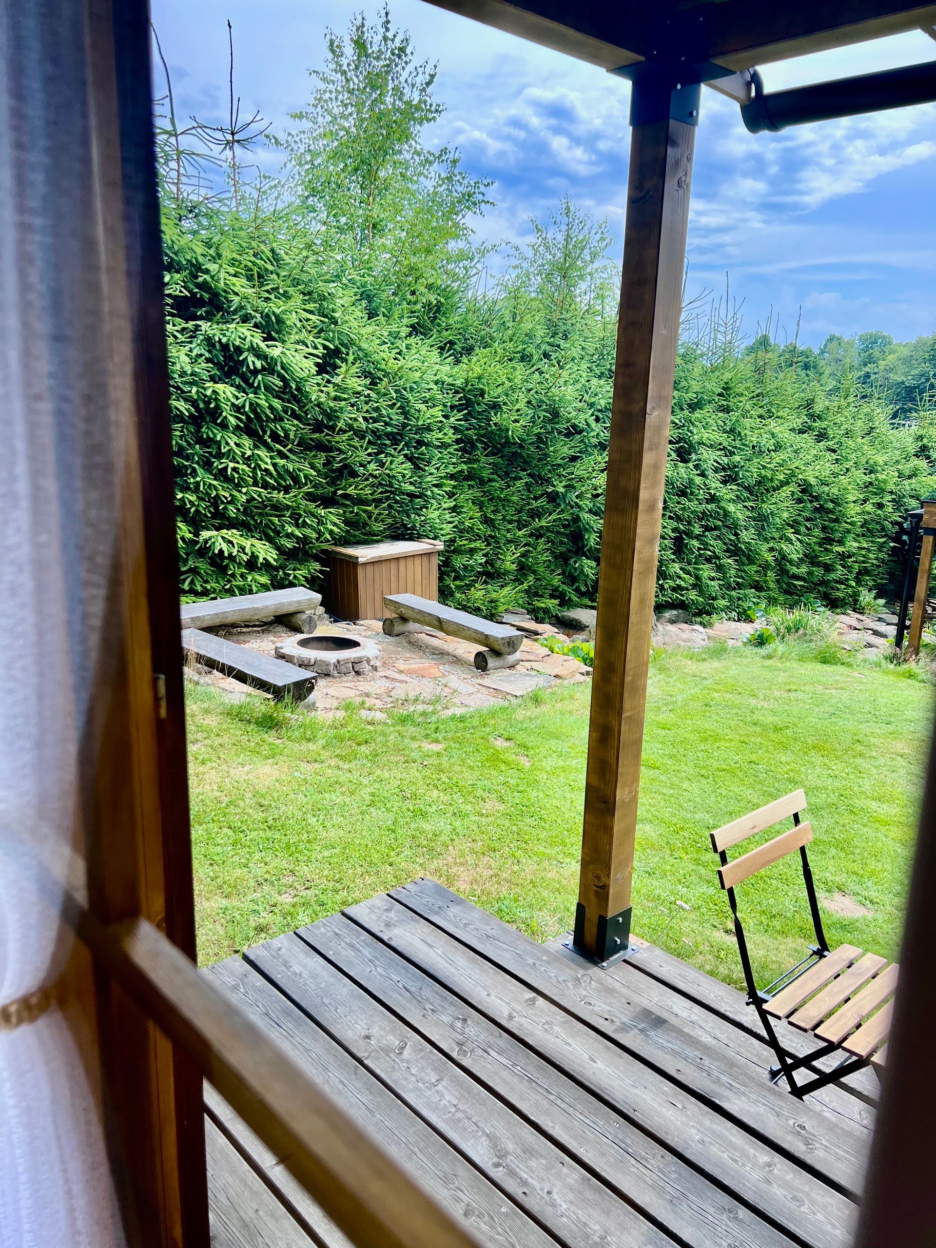 Wooden porch with a view of a fire pit and trees.