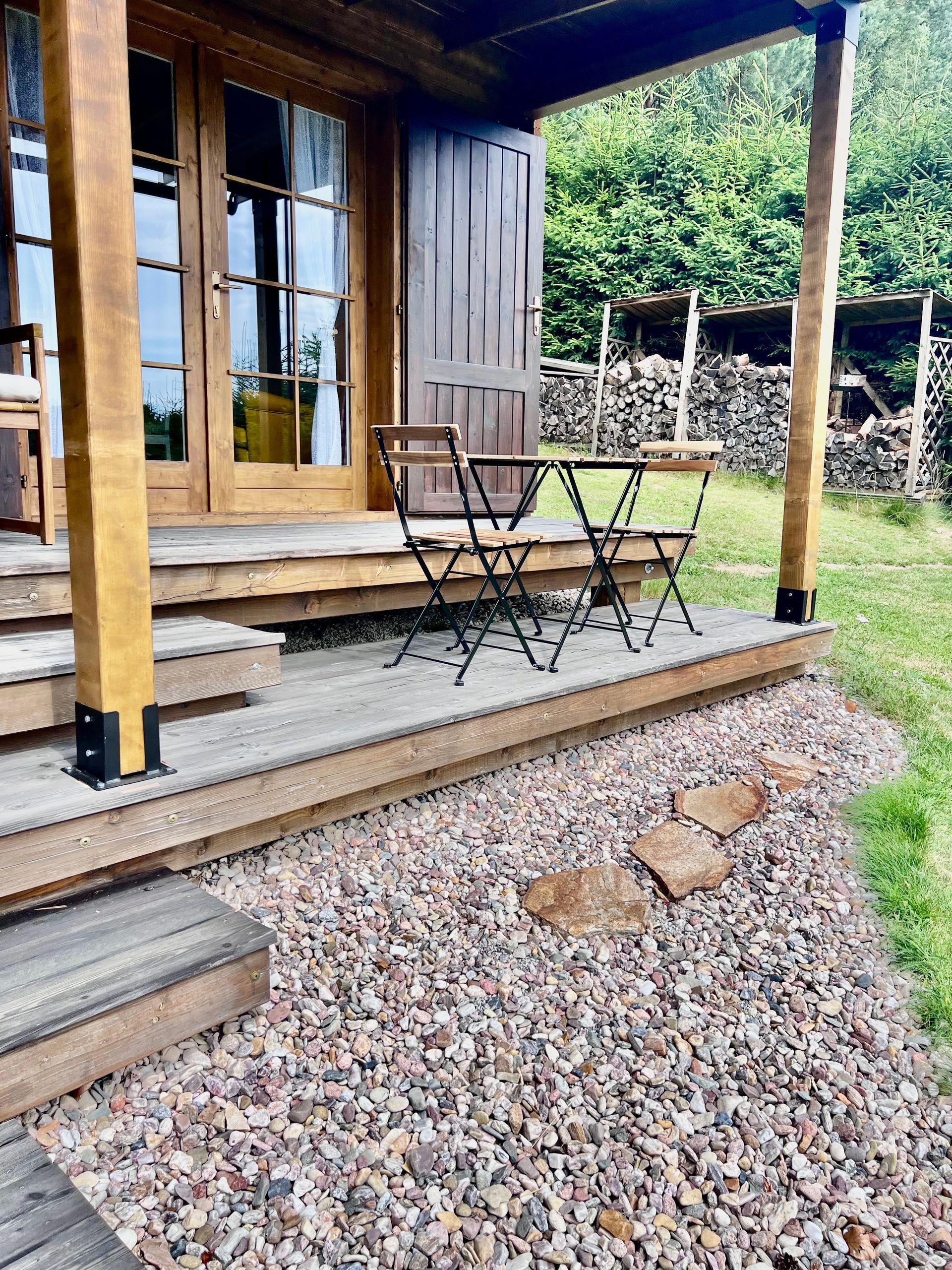 Wooden cabin porch with a small table and chairs, gravel border.