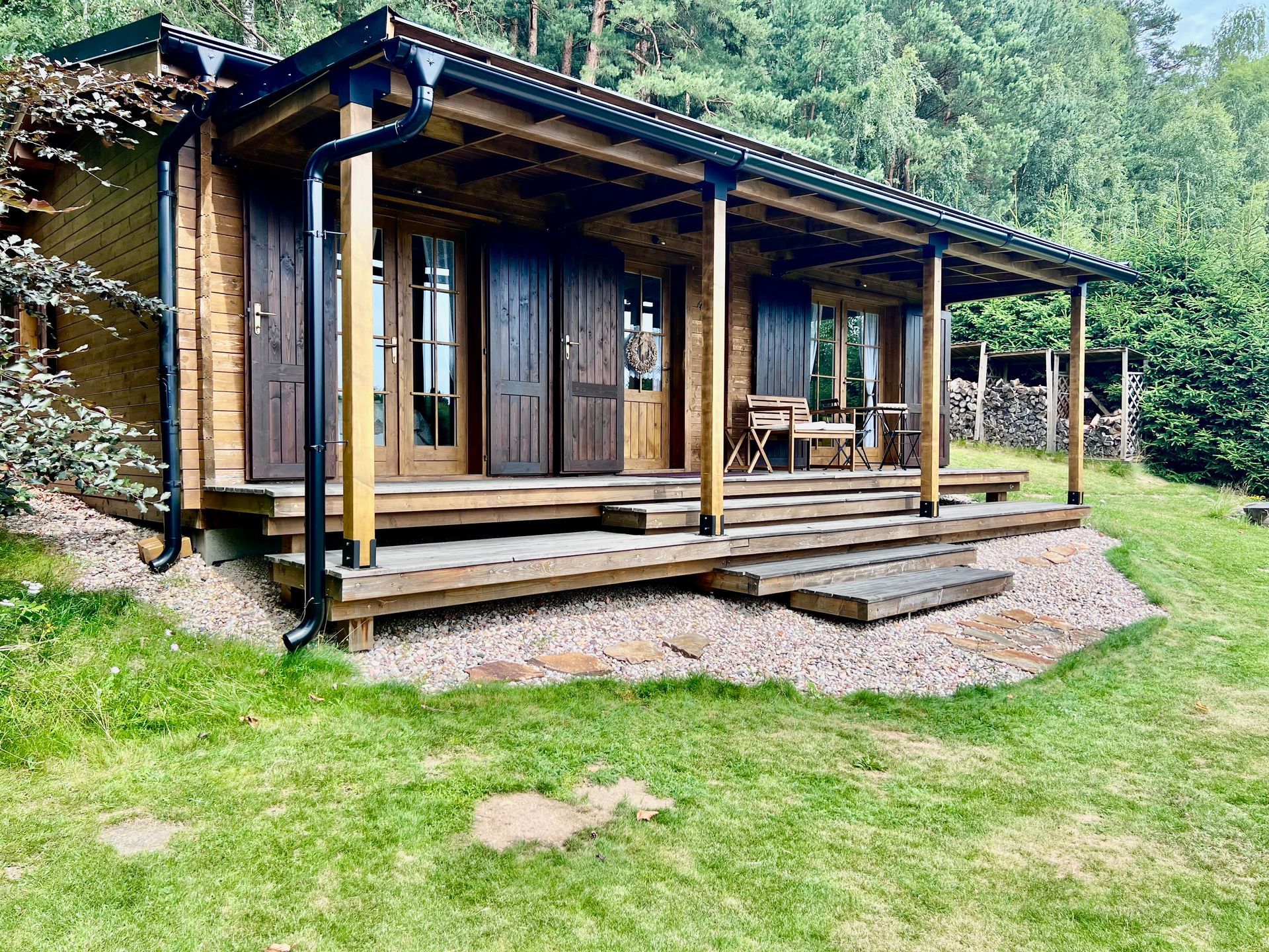 Wooden cabin with porch, brown shutters, and green surroundings.