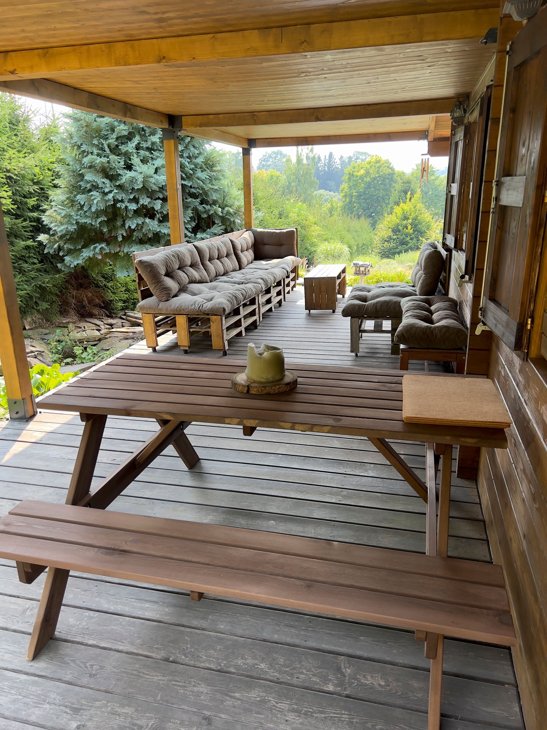 Wooden outdoor seating area with a picnic table and benches, overlooking a green landscape.