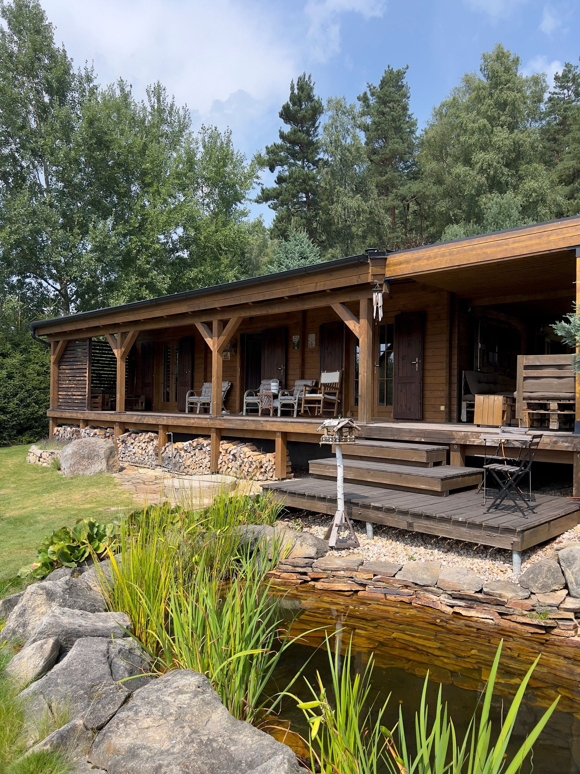 Wooden cabin with porch, overlooking a pond and greenery.