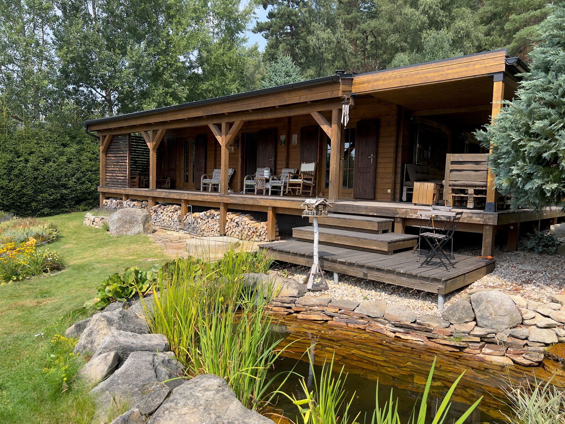 Wooden cabin with porch and pond in a grassy yard.