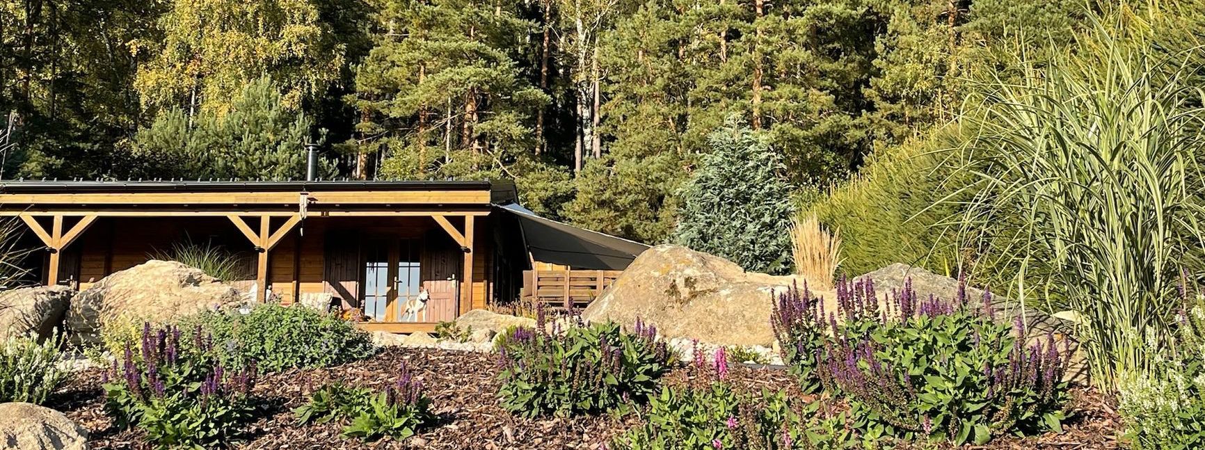 Wooden structure in a garden setting with a backdrop of trees. Green foliage in the foreground.
