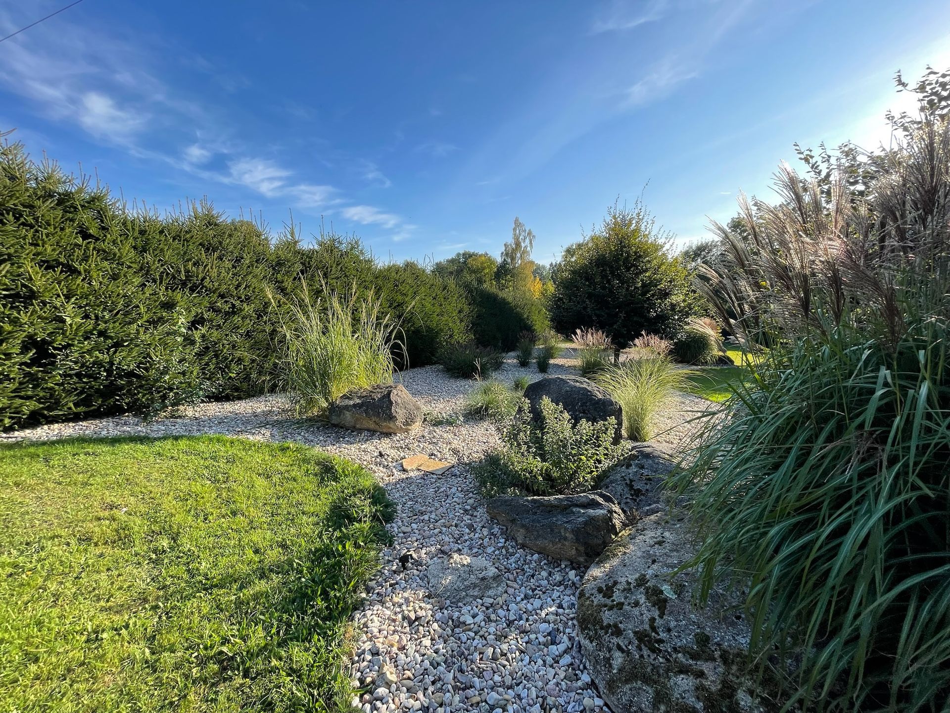 Green lawn, rock garden, trees under a blue sky.