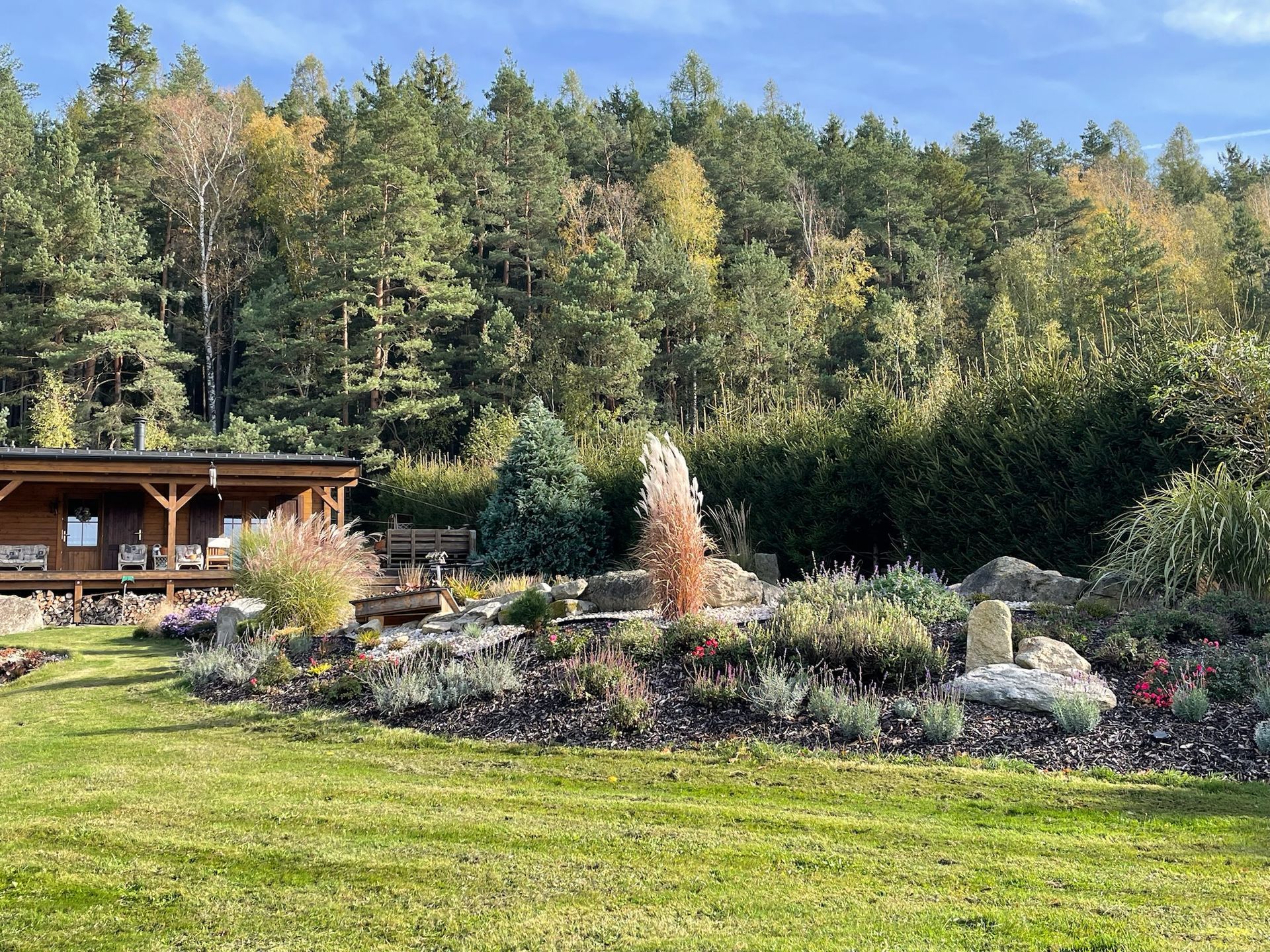 A wooden cabin with a colorful garden in front of a forest.