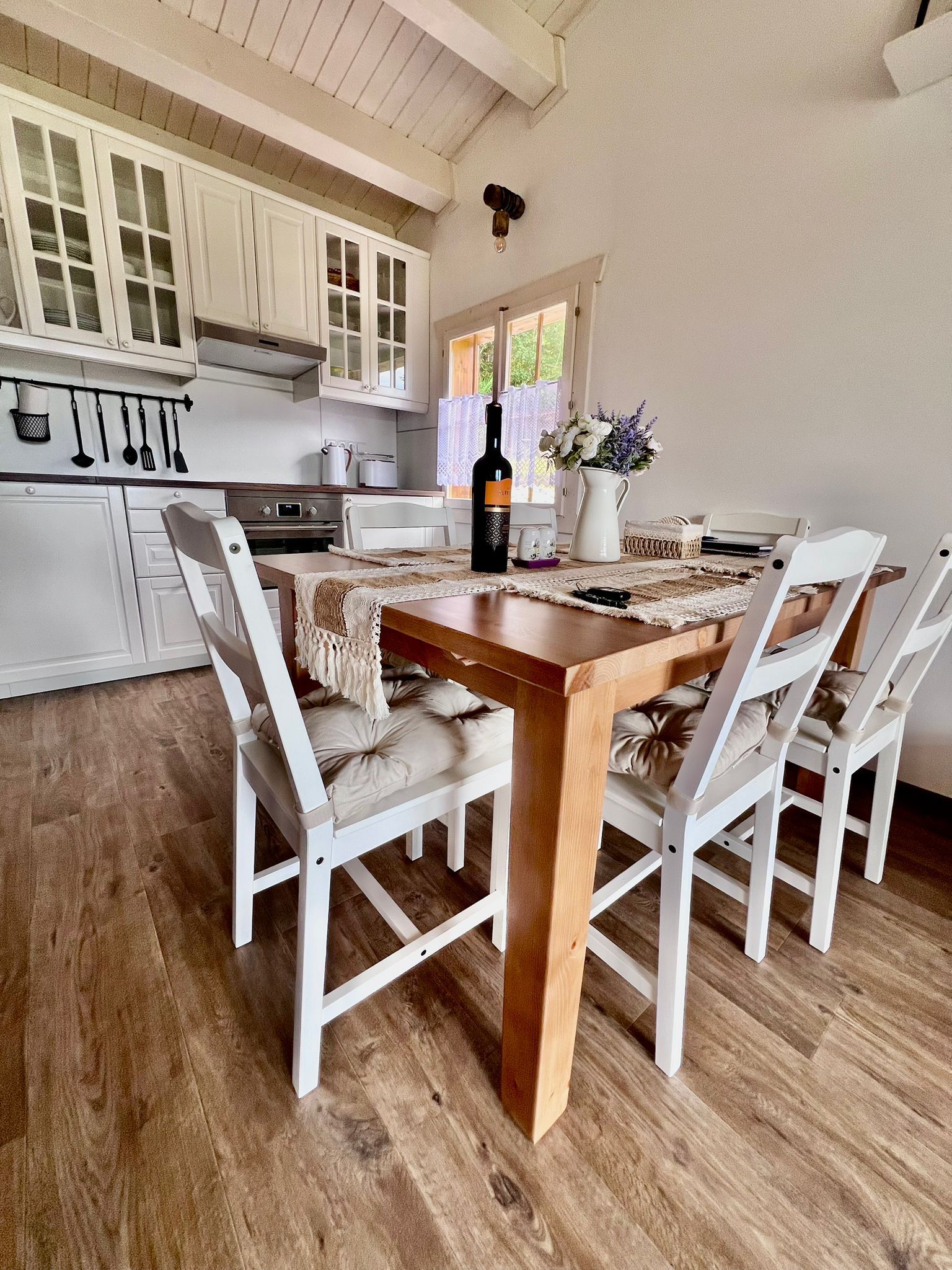 A small dining area with a wooden table, white chairs, and a kitchen.