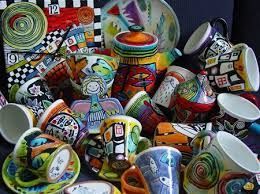 Colorful hand-painted ceramic mugs, teacups, a teapot, clock, and angel figurine in a vibrant display.