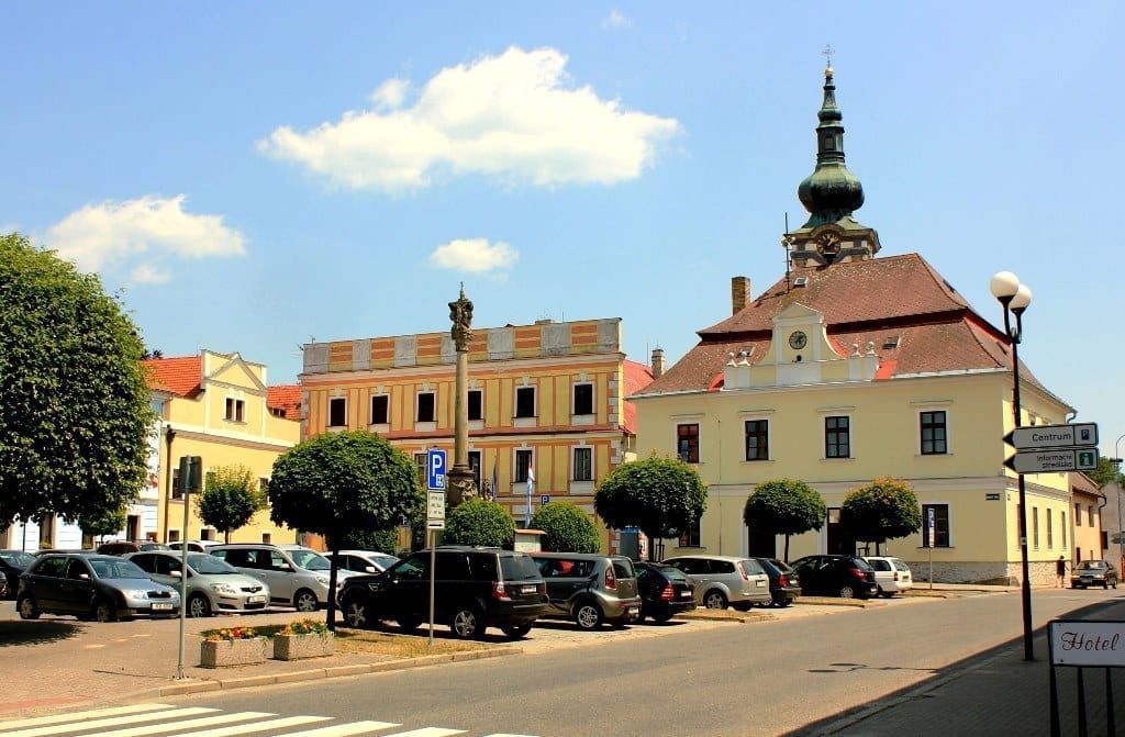 Town square with parked cars, buildings, and a clock tower on a sunny day.