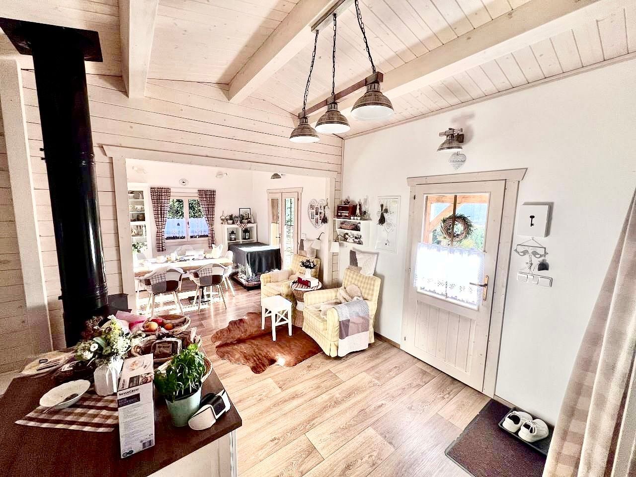 Útulný interiér chaty s dřevěnými podlahami, krbem a posezením; v pozadí viditelná jídelna.