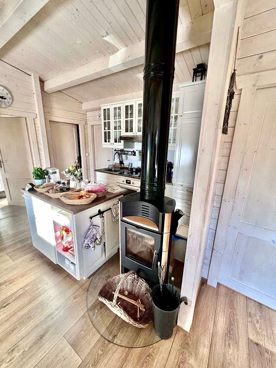 Cozy kitchen with wood stove, island counter, and white cabinets. Wooden floors and paneling.