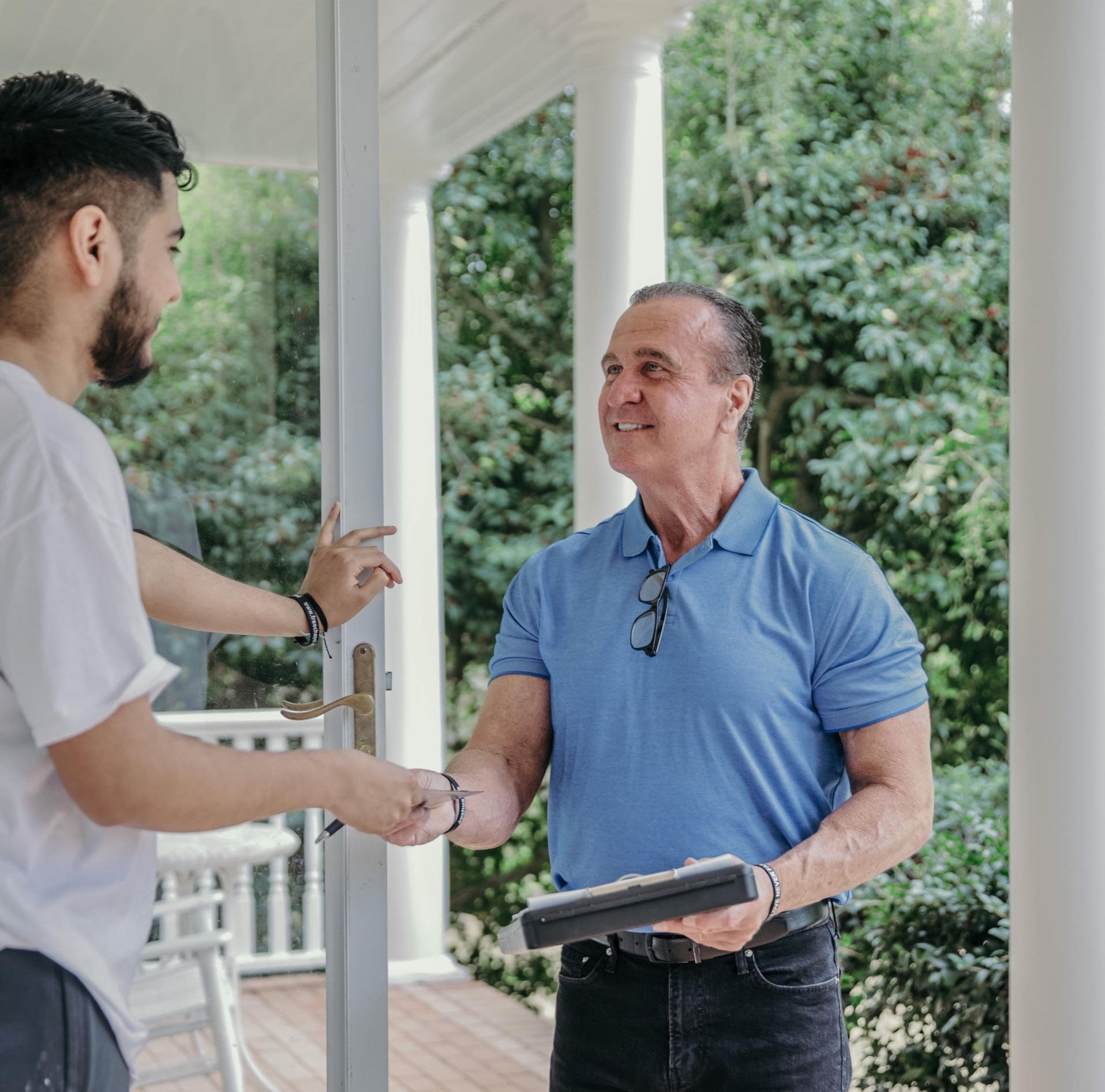 A man is standing on a porch talking to another man.