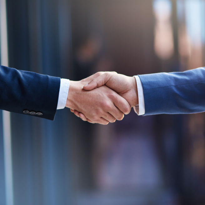 Two men in suits are shaking hands in a hallway.