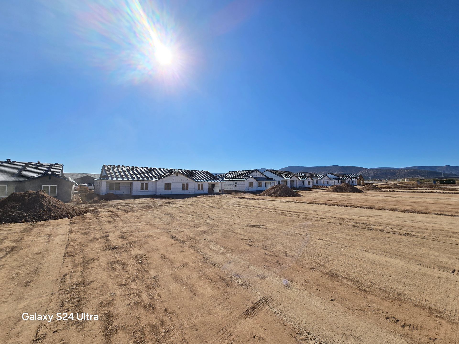 A group of houses are being built in a dirt field.