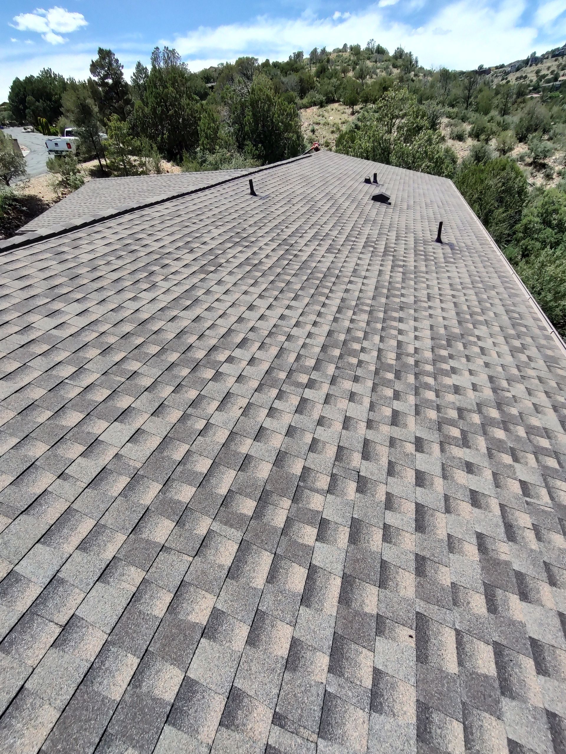 A man wearing a hard hat is standing on a roof looking at a clipboard.