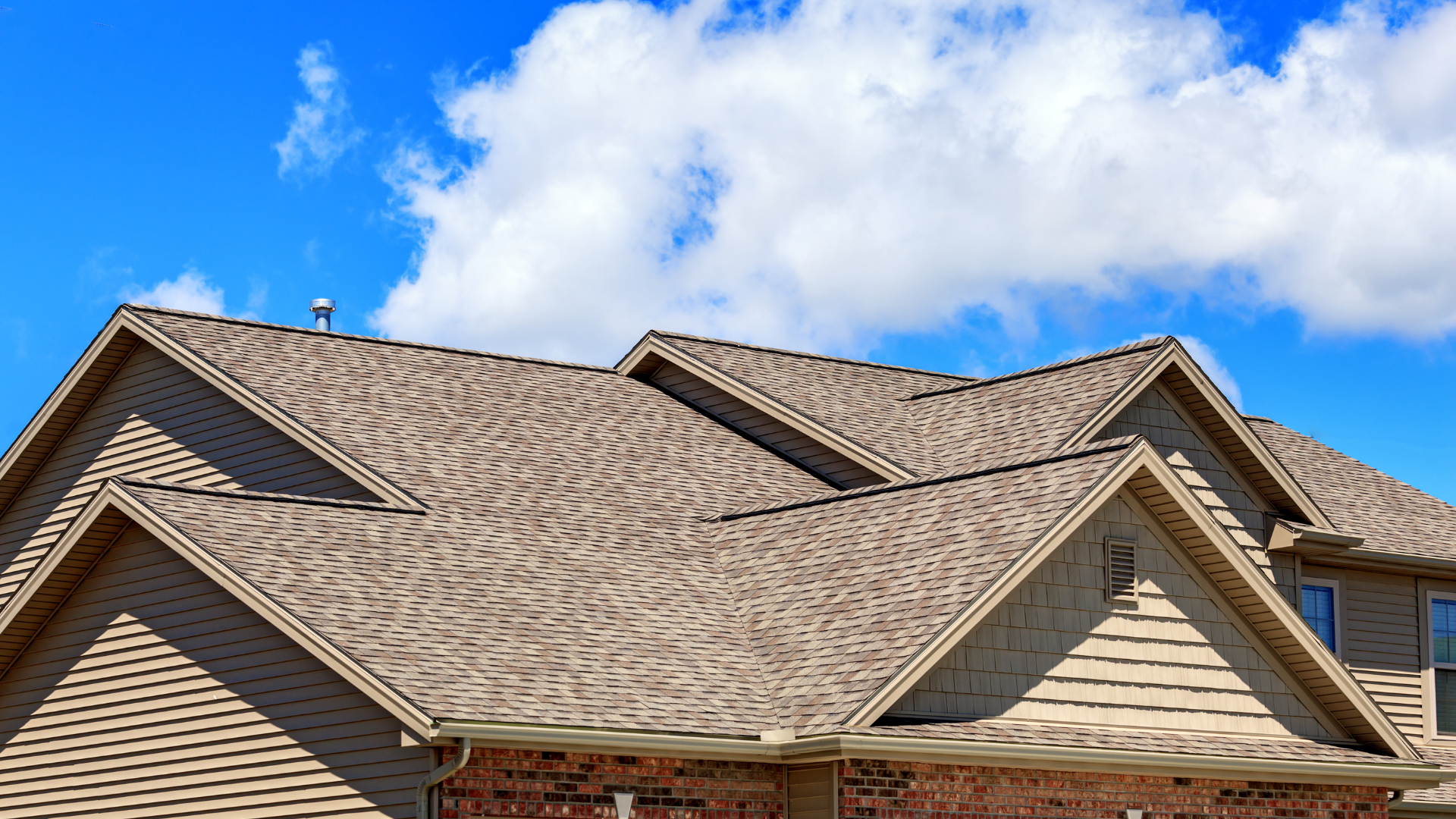 The roof of a house with a blue sky and clouds in the background.