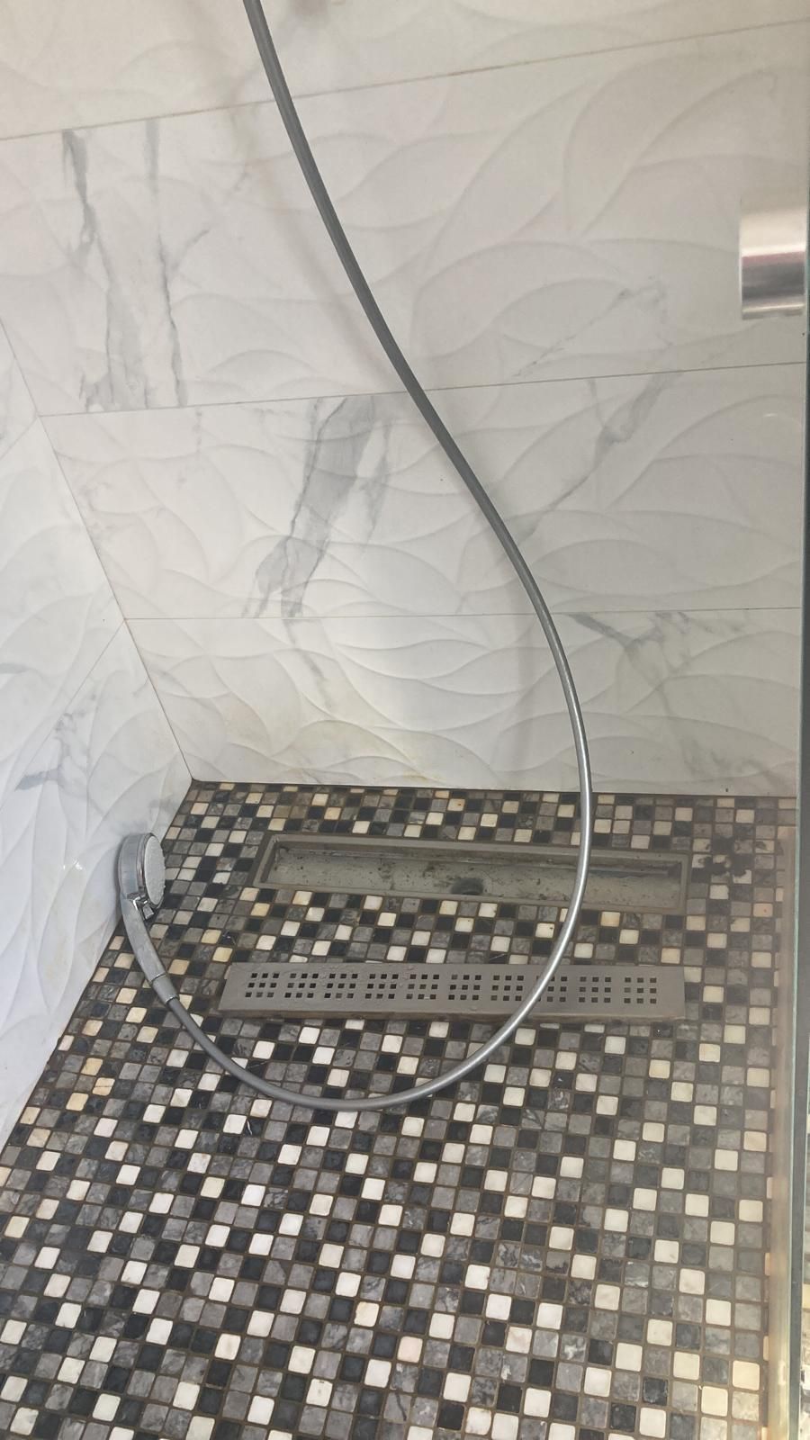 Une cabine de douche avec un sol en mosaïque et une pomme de douche.