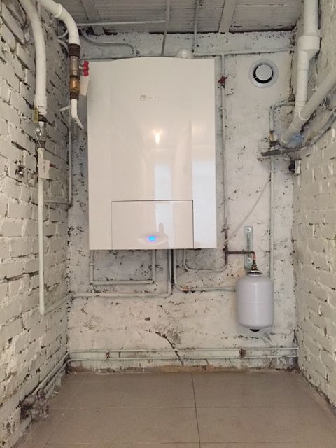 Une chaudière blanche est montée sur un mur de briques blanches