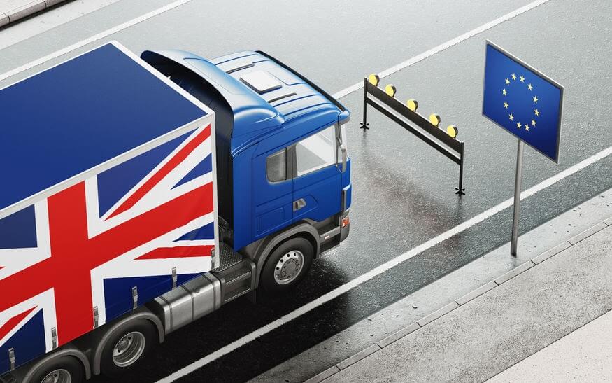 Lorry with British flag on the side of it stopped by a gate with the European Union flag next to it.