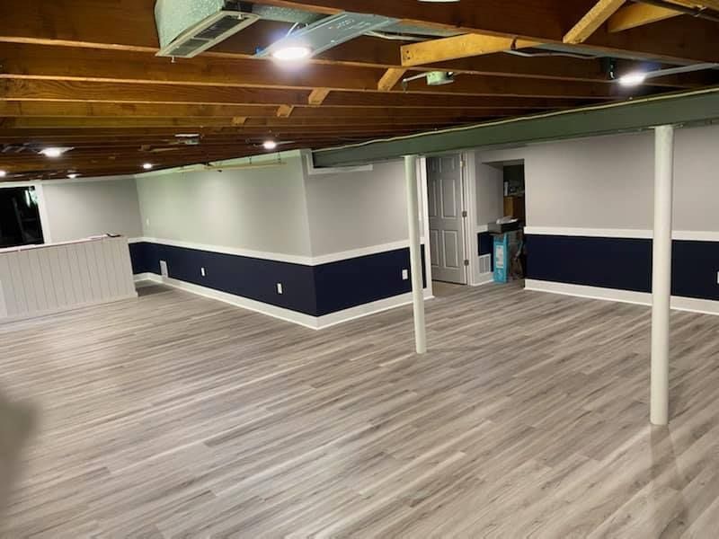 An empty basement with a wooden floor and white cabinets.