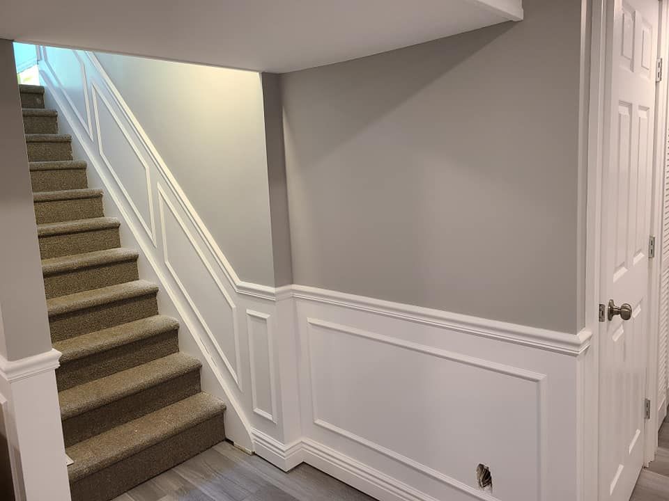 A staircase in a basement with carpeted steps and a white railing.