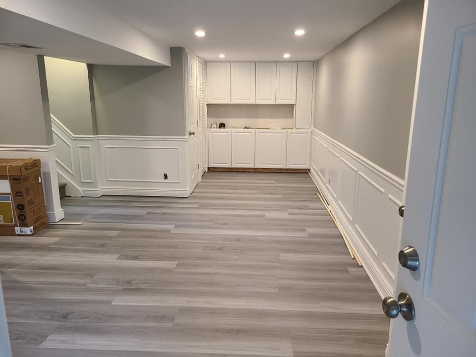 An empty basement with a wooden floor and white cabinets.