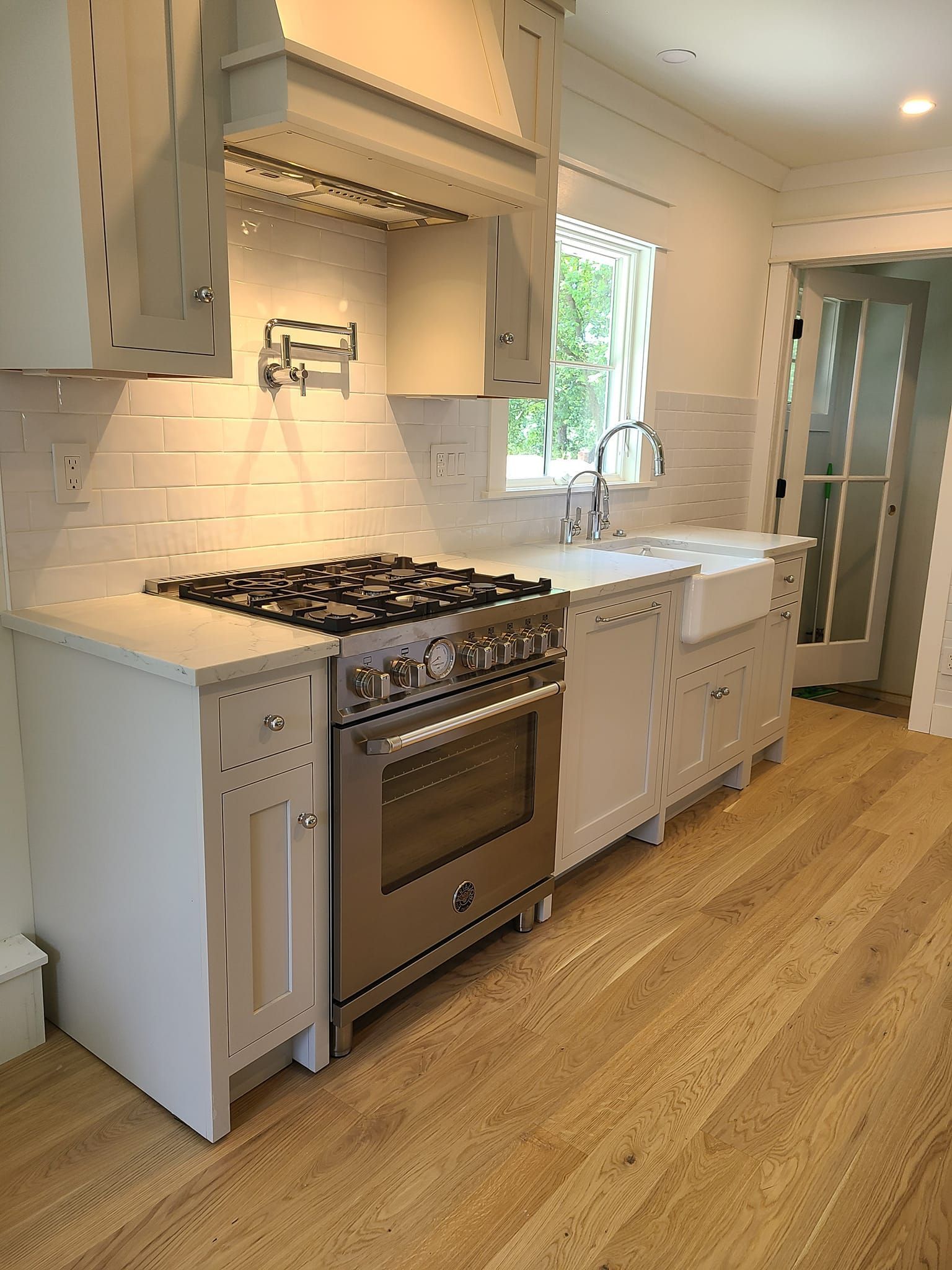 A kitchen with white cabinets , a stove , a sink , and a window.