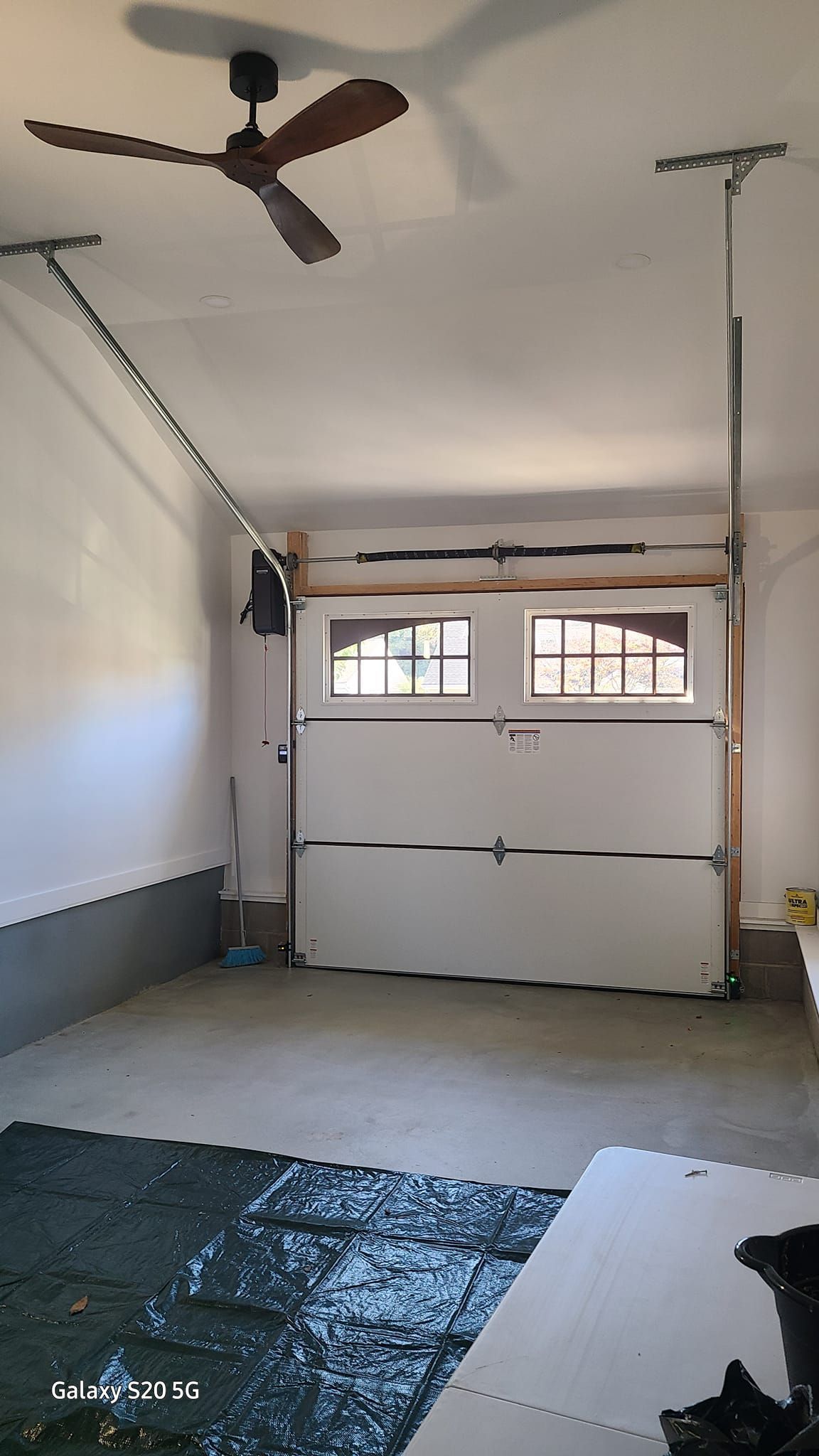 An empty garage with a ceiling fan and a white garage door.