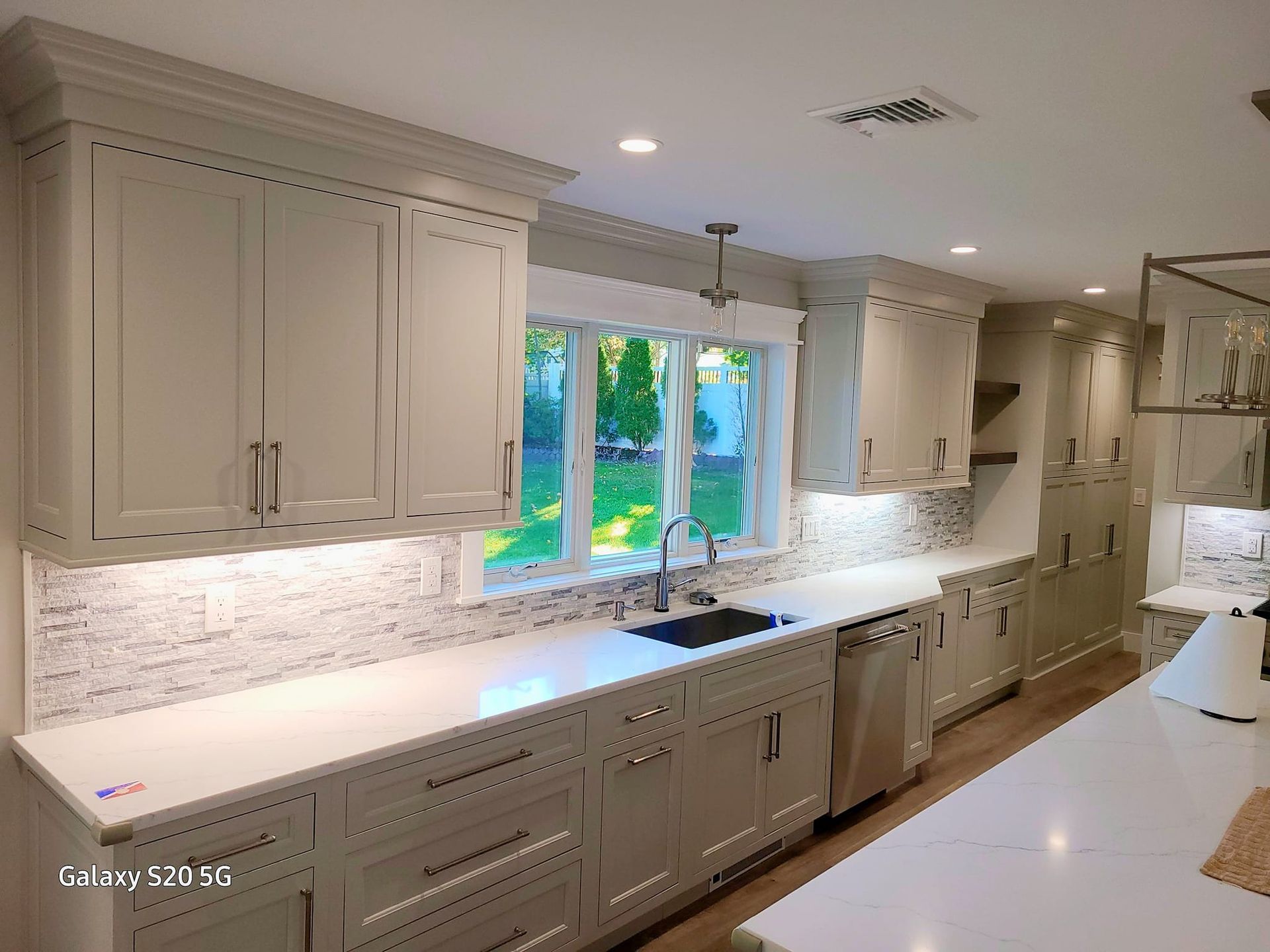 A kitchen with white cabinets , white counter tops , a sink and a window.