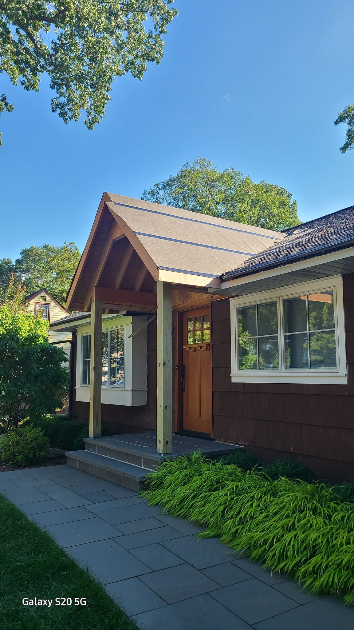 A brown house with a porch and a roof on a sunny day.