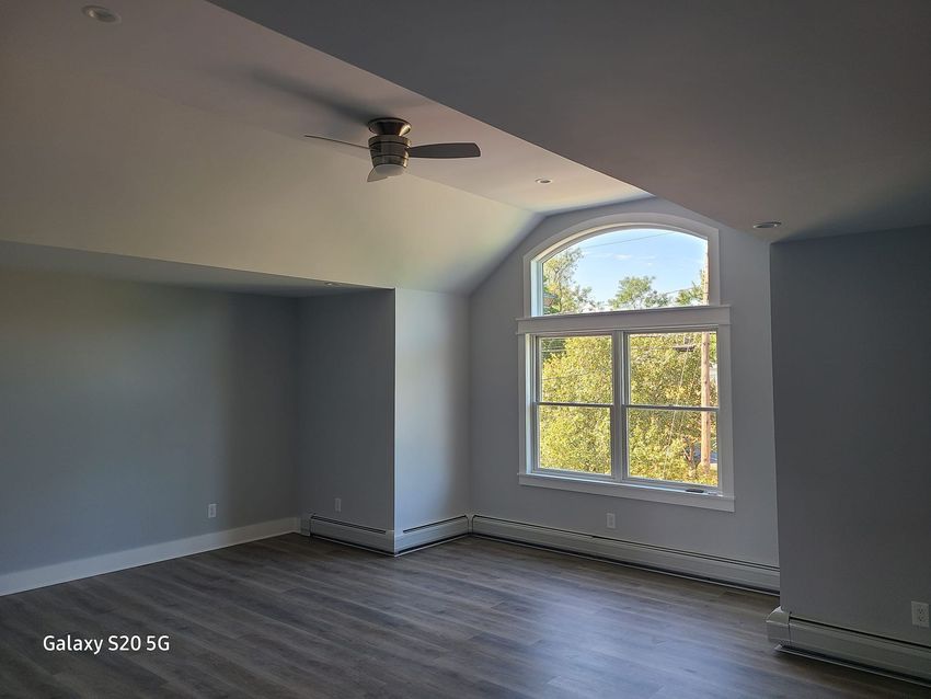 An empty room with a ceiling fan and a large window.