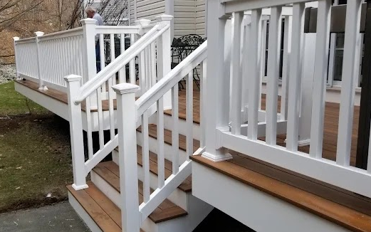 White railing and stairs leading up to a wooden deck. Person in background.